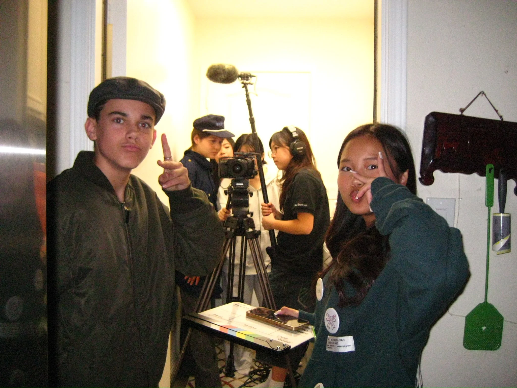 Group of young filmmakers posing around a video camera, tripod, and boom microphone indoors.