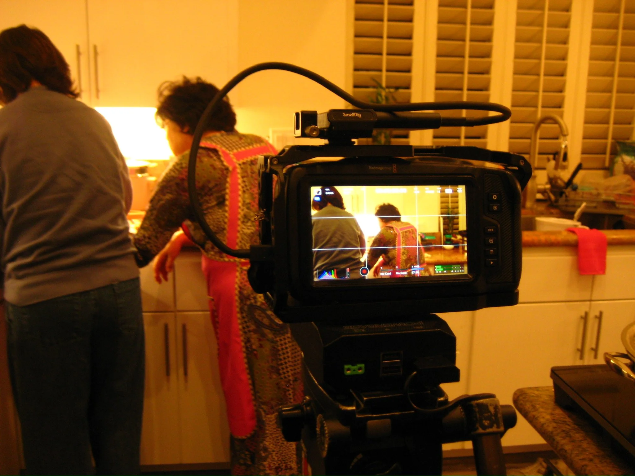 Professional video camera filming two people in a warmly lit kitchen.