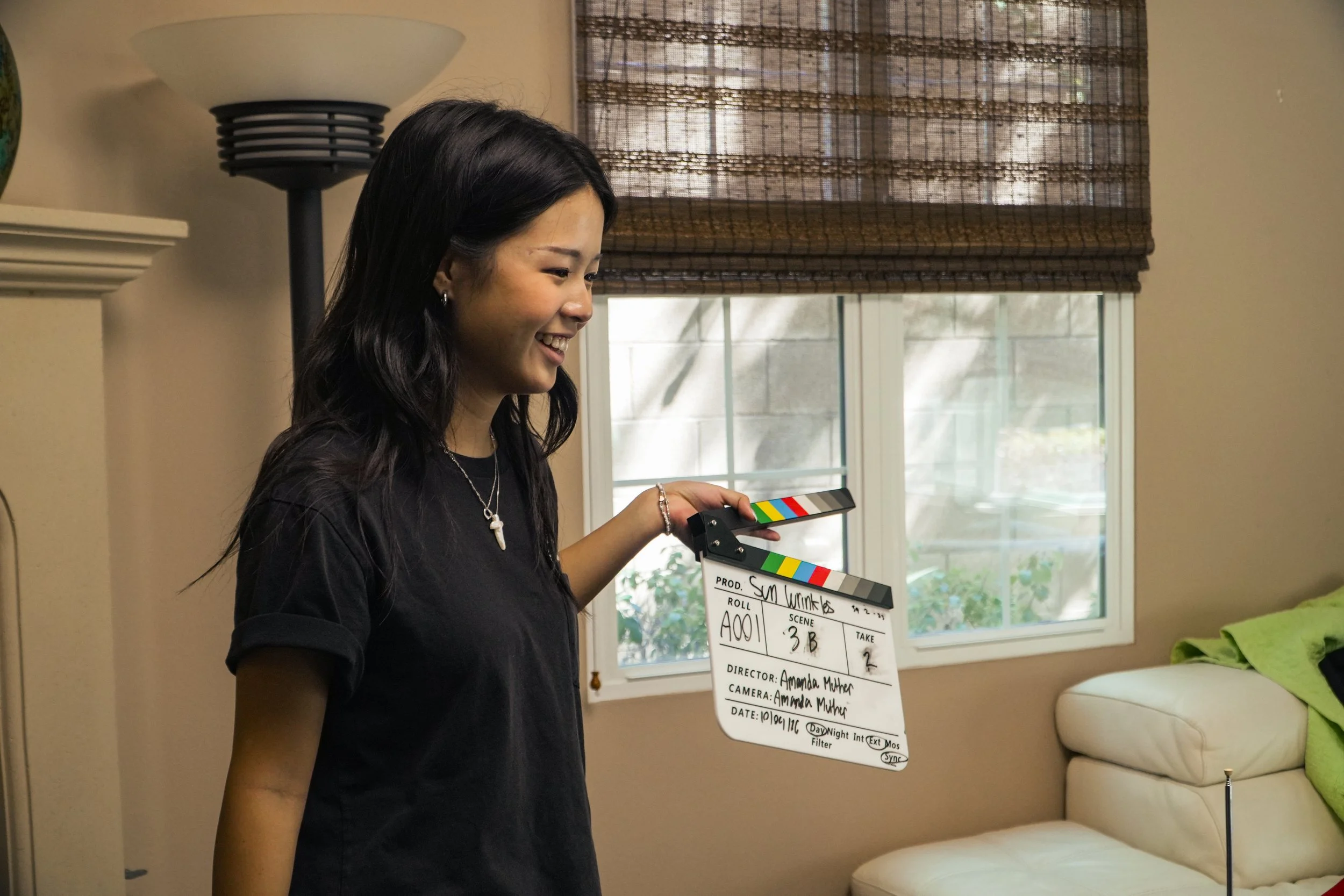 Smiling woman holding a film clapperboard in a living room