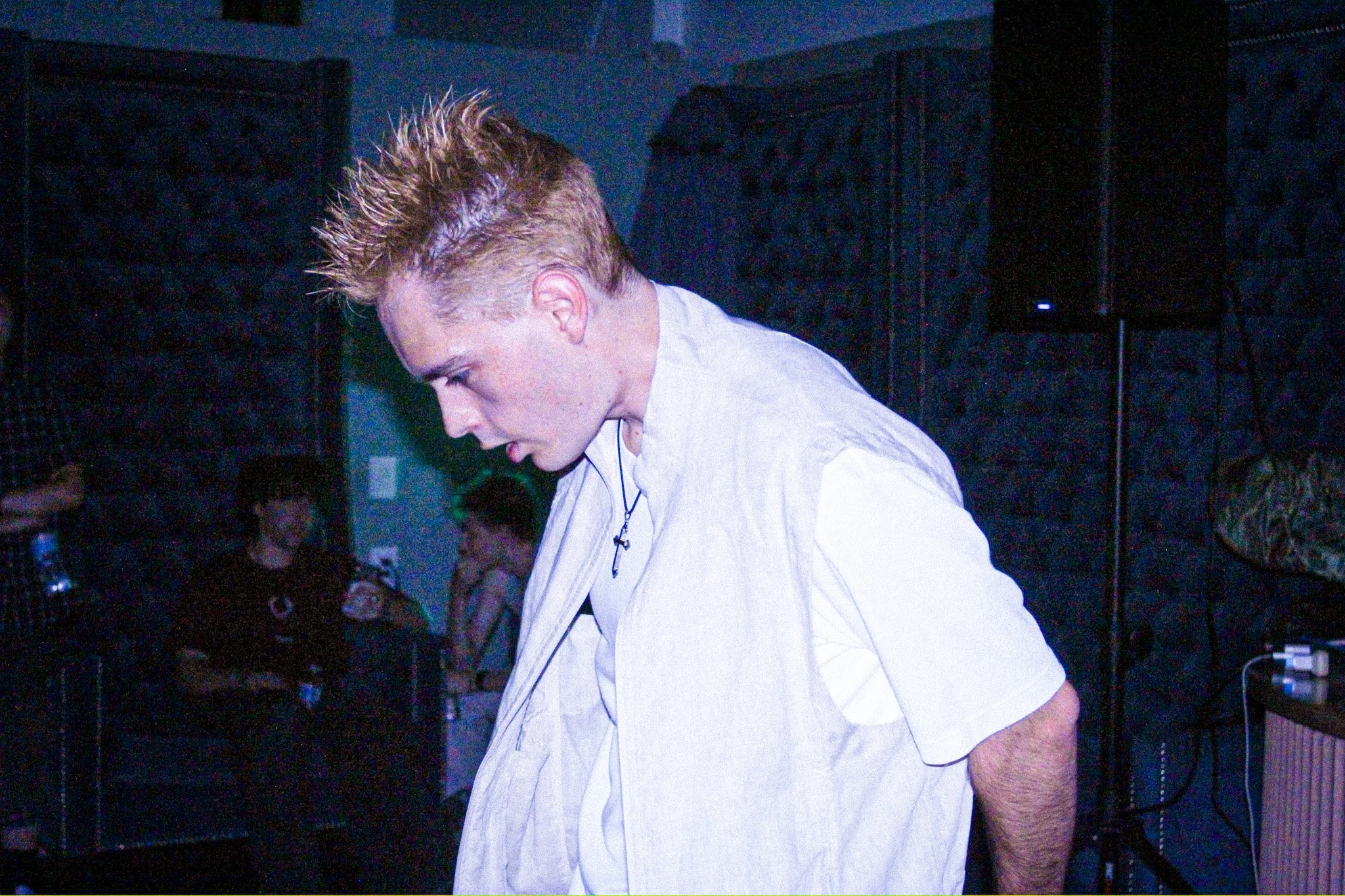 Blond man in a white shirt leaning forward at a dimly lit concert or nightclub.