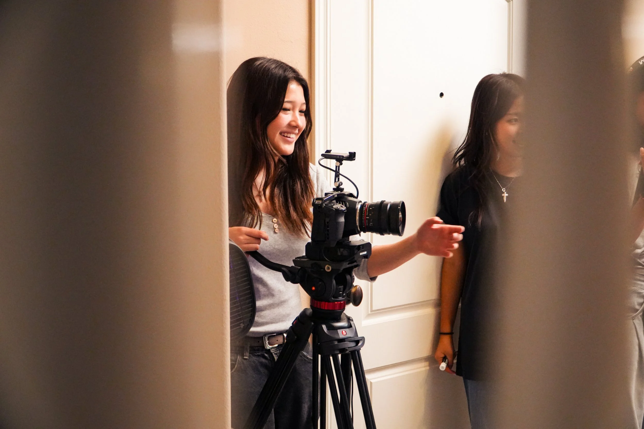 Two women filming indoors with a professional camera mounted on a tripod