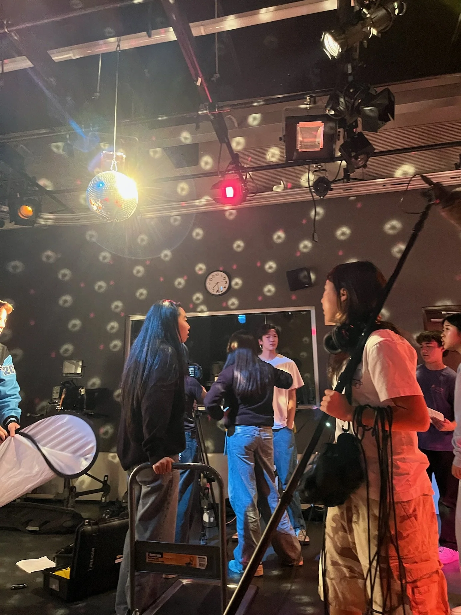 Group of people gathered in a nightclub beneath colorful stage lights and a disco ball.