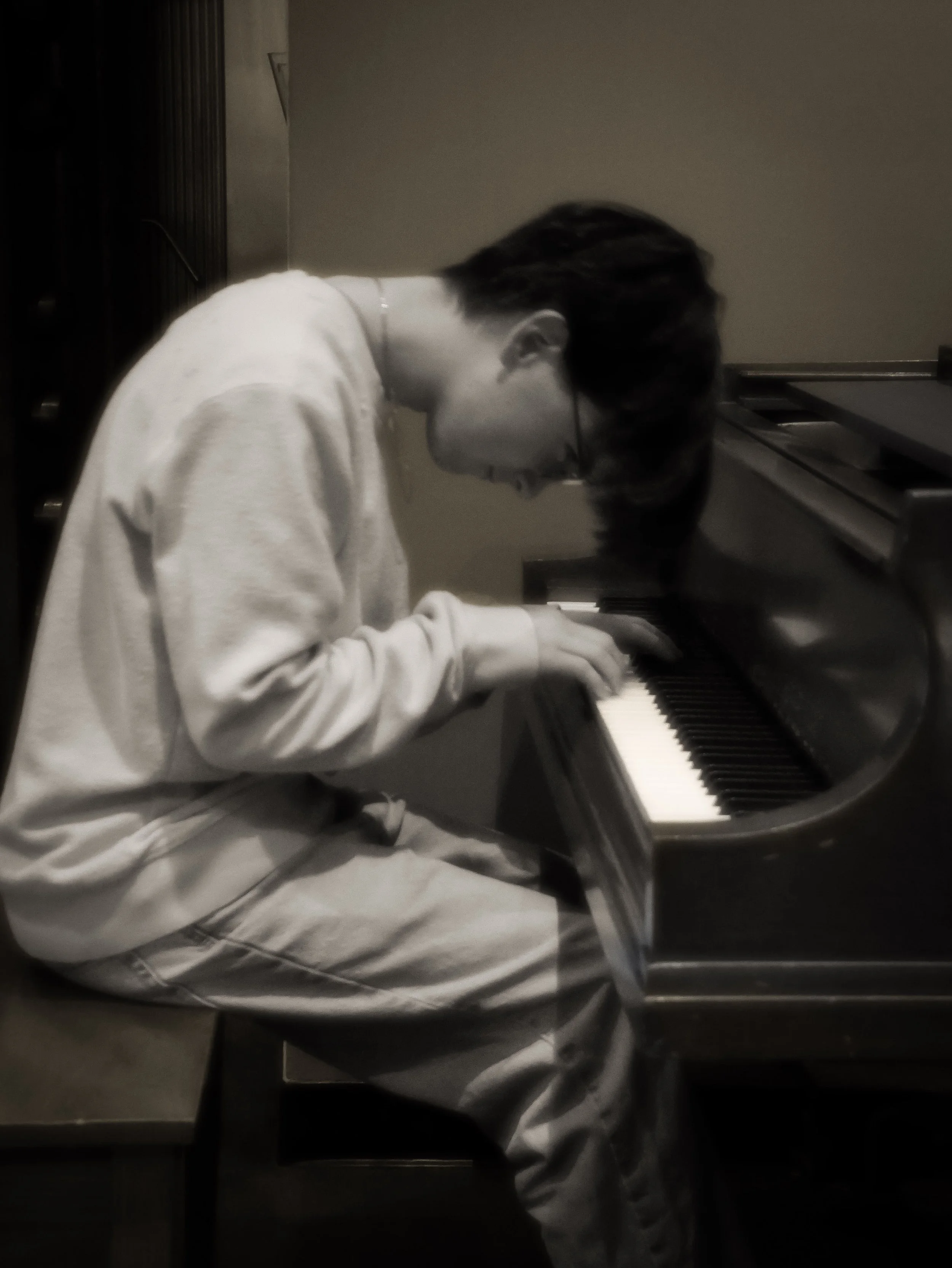 Black-and-white photo of a pianist playing an upright piano in a dimly lit room