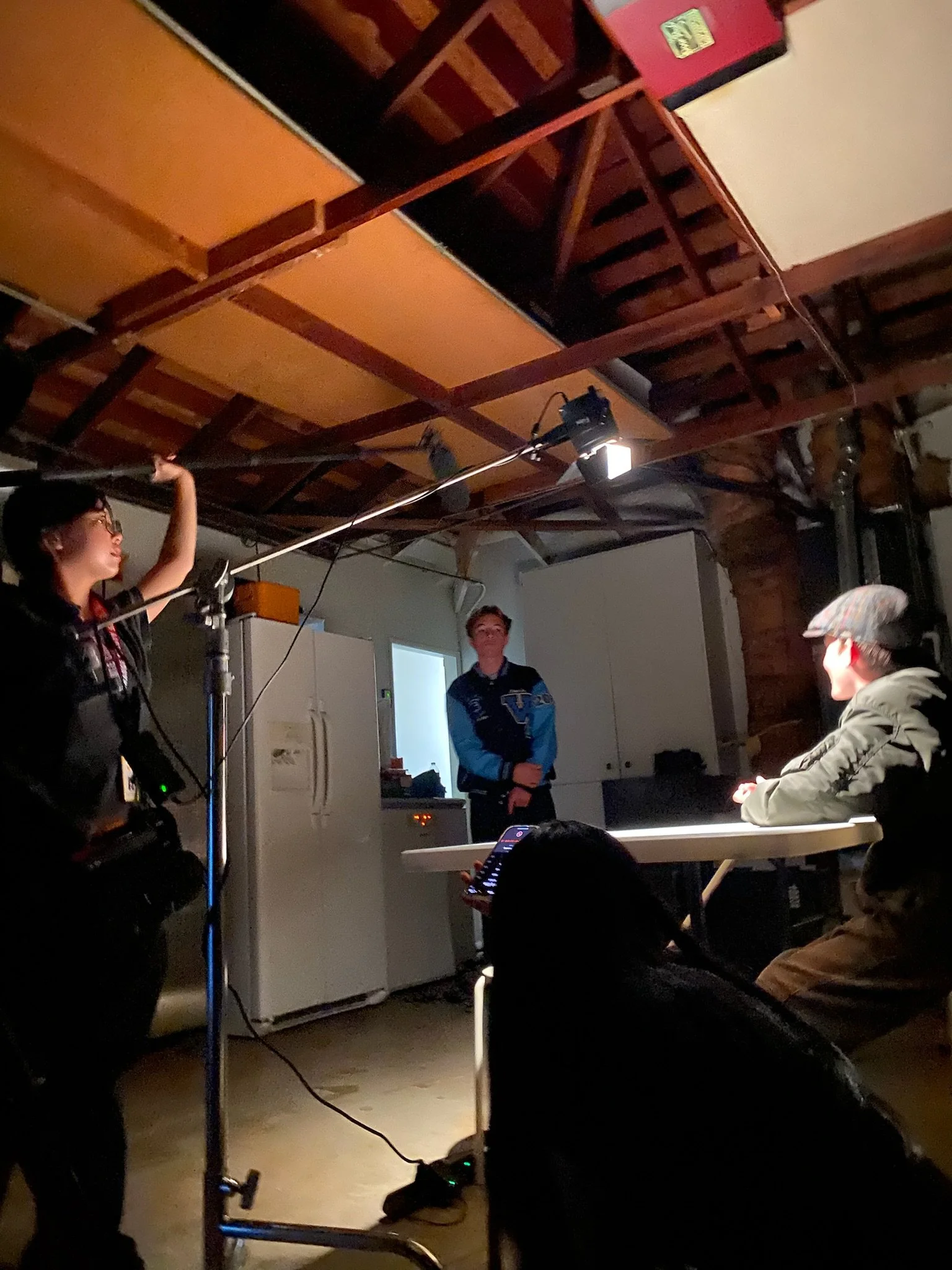 Film crew recording a classroom scene with actors, cameras, lighting equipment, and a boom microphone.
