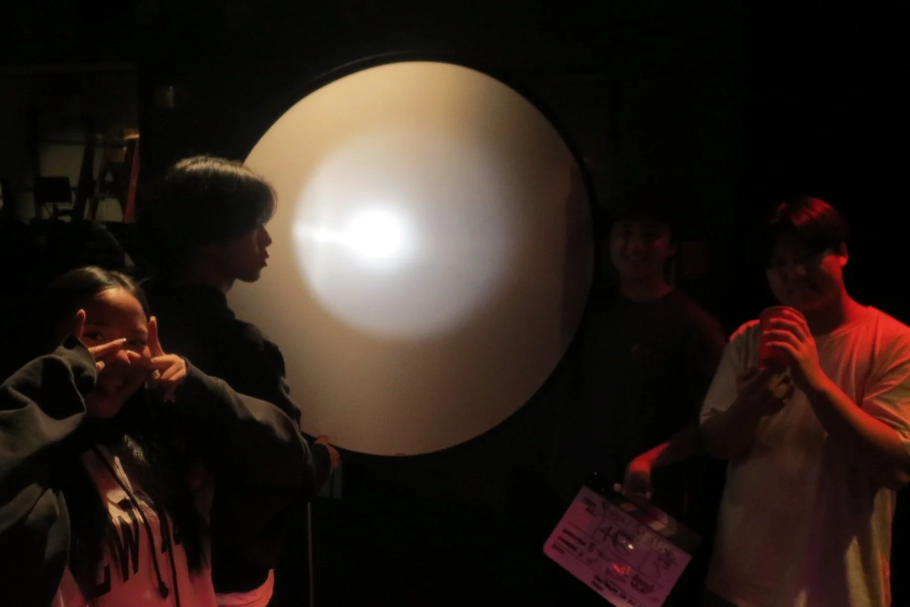 Group of people posing around a large illuminated white sphere in a dark room