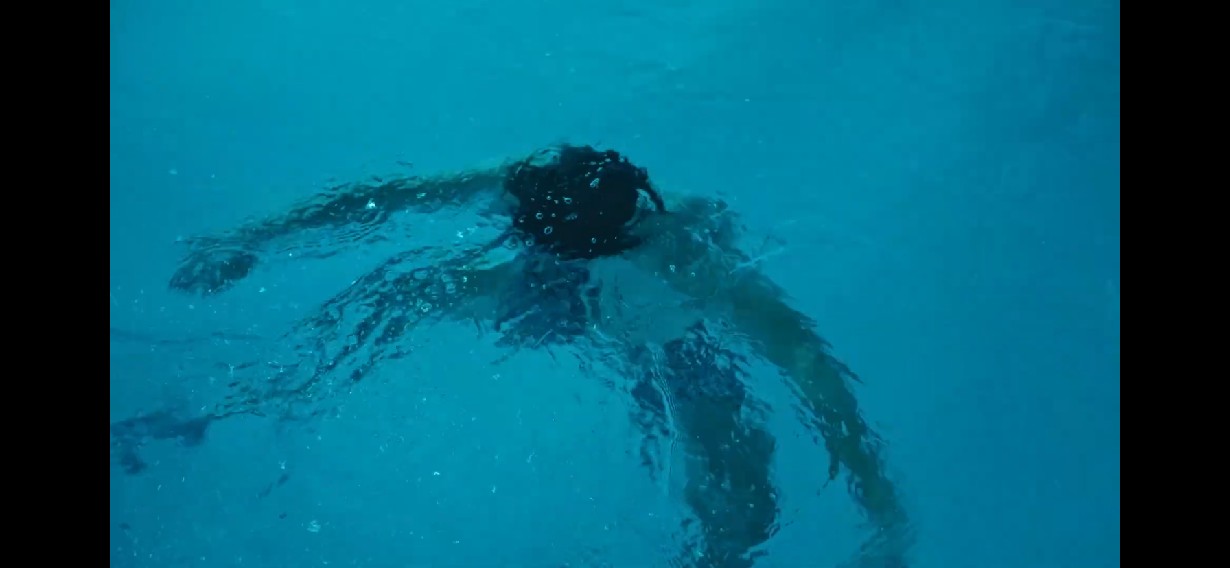 Person swimming underwater in a blue pool