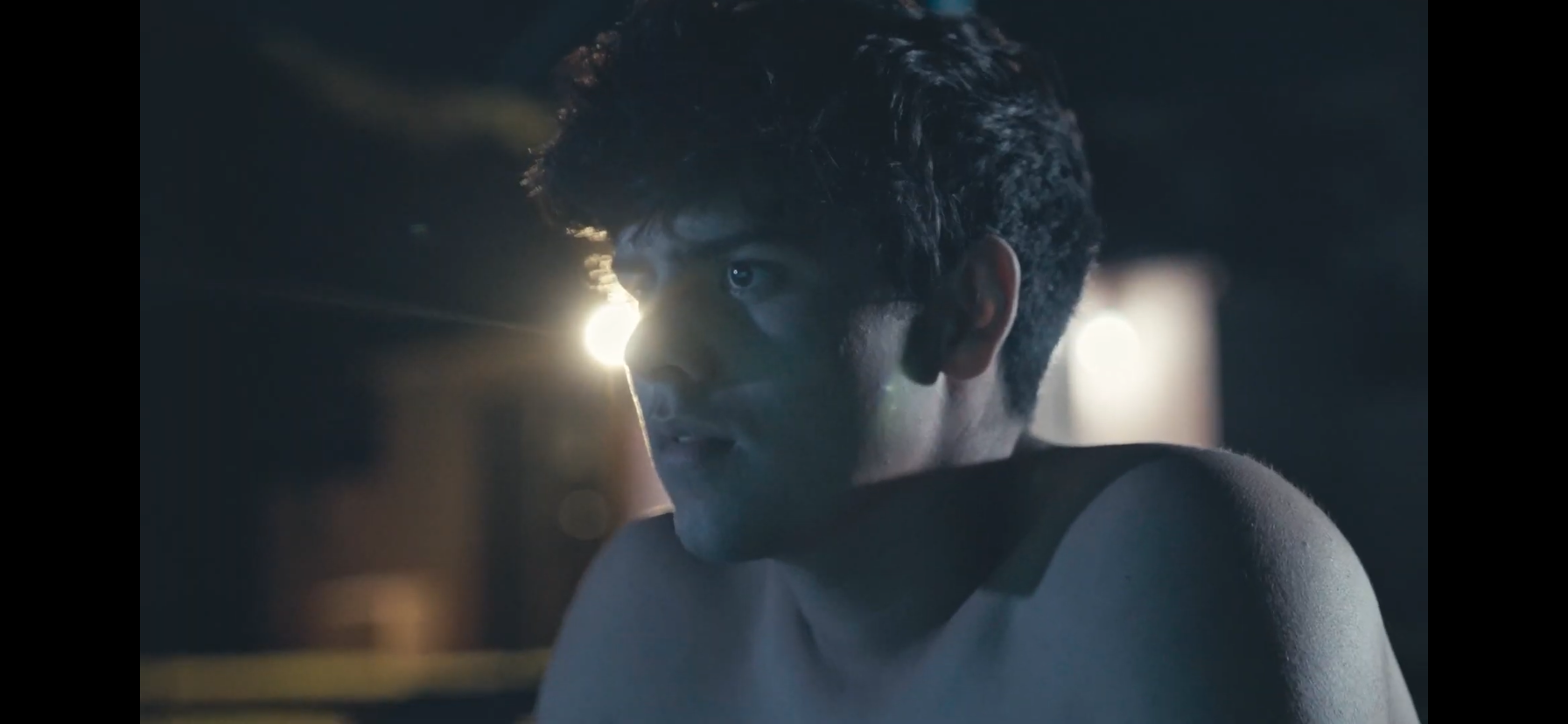 Close-up of a young man in a dimly lit room, illuminated by dramatic blue and warm backlighting.