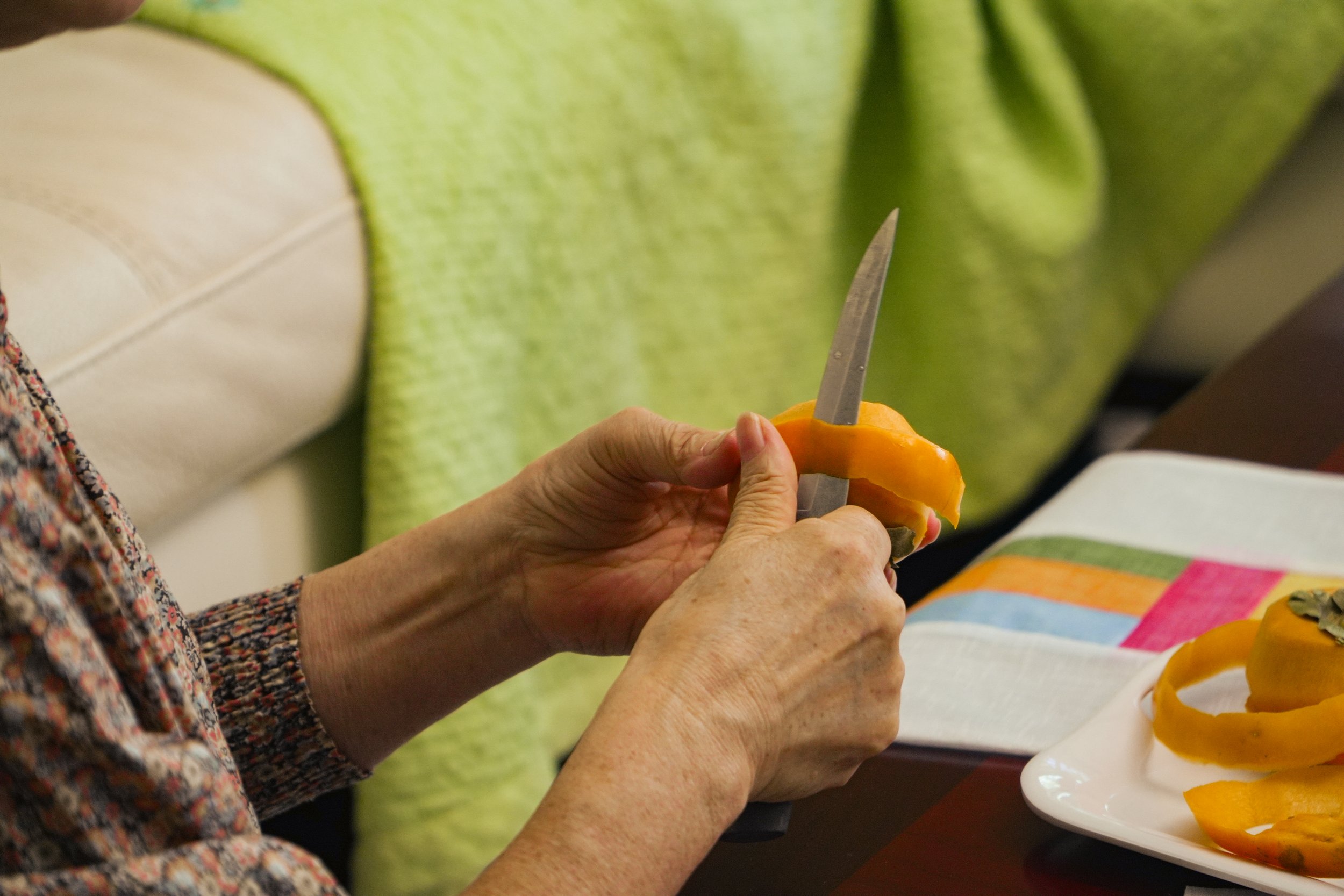 Person peeling an orange with a knife over a plate of orange peels