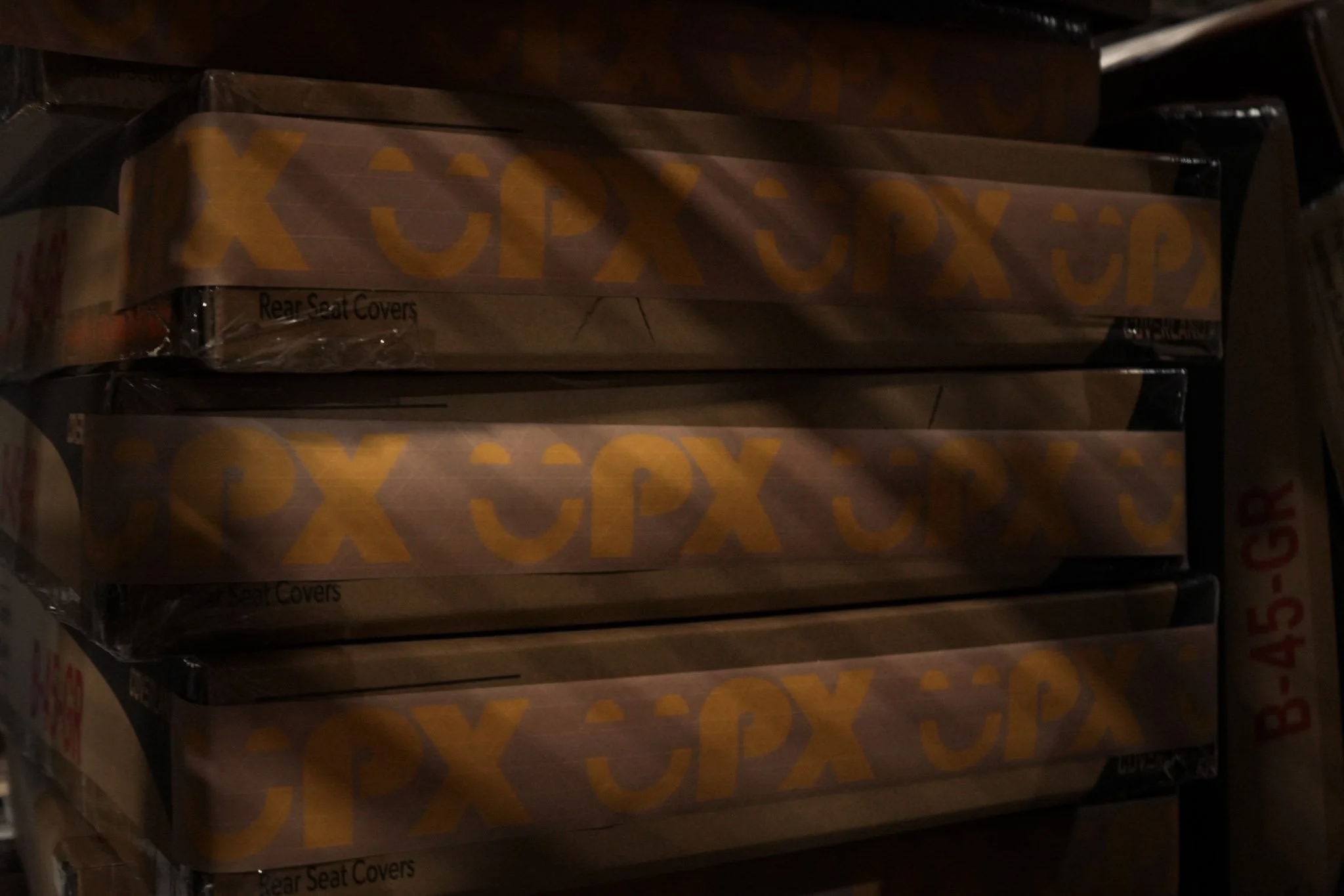 Close-up of stacked cardboard boxes labeled "Rear Seat Covers" in a dim storage area