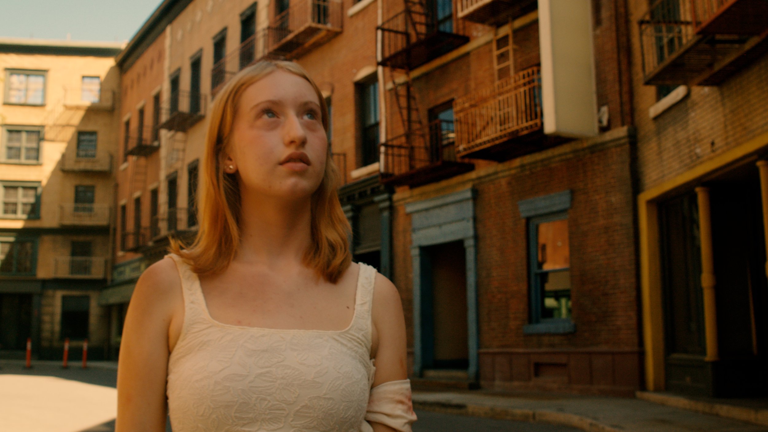 Young woman looking up in a sunlit urban alley lined with brick buildings and fire escapes