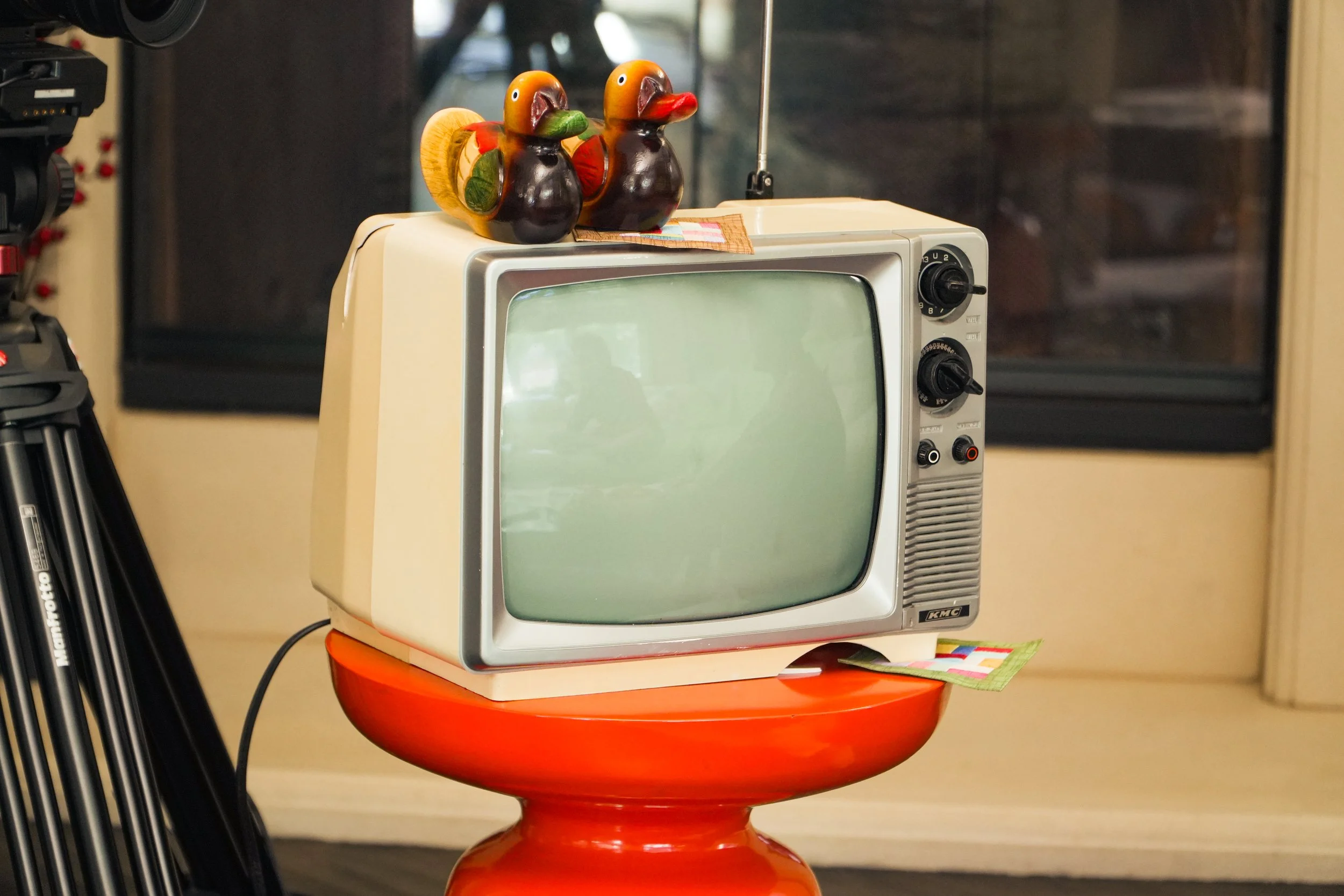 Vintage KMC television with two colorful wooden duck figurines on top, displayed on a red pedestal table