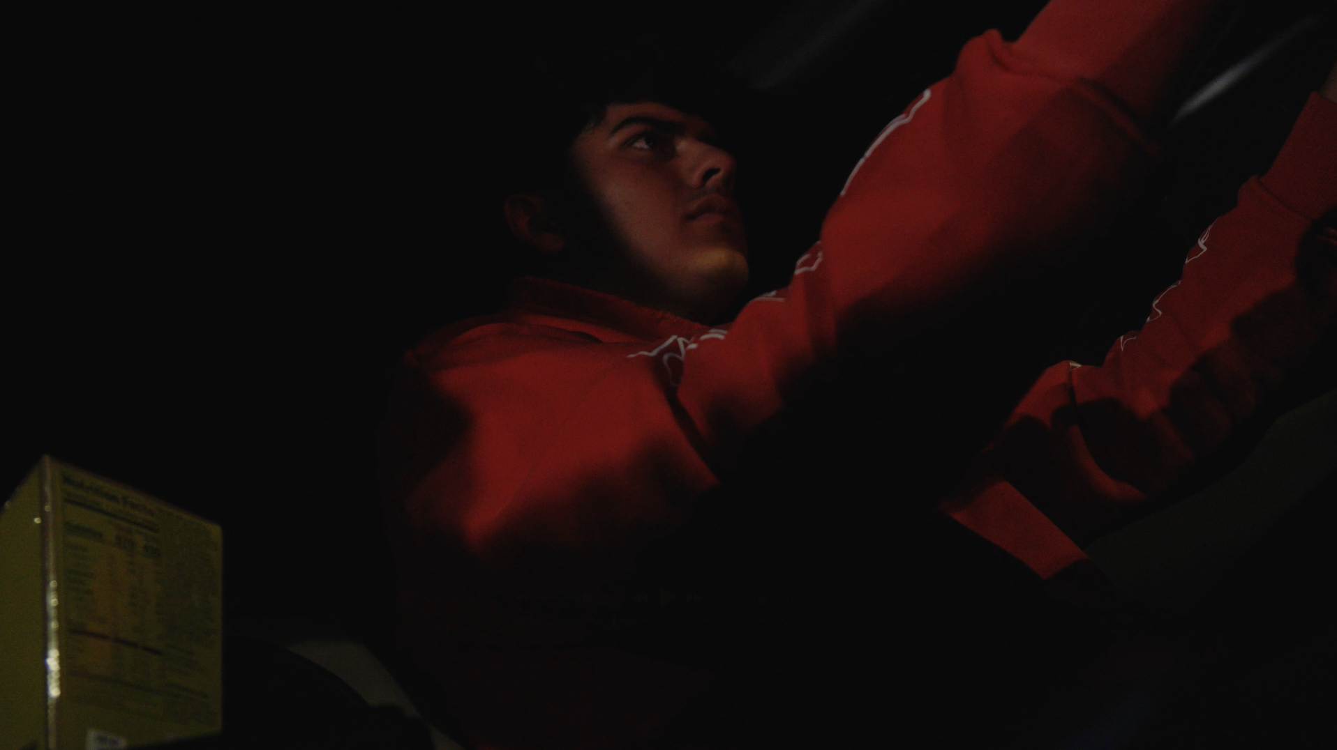Person in a red jacket seated in a dimly lit vehicle at night