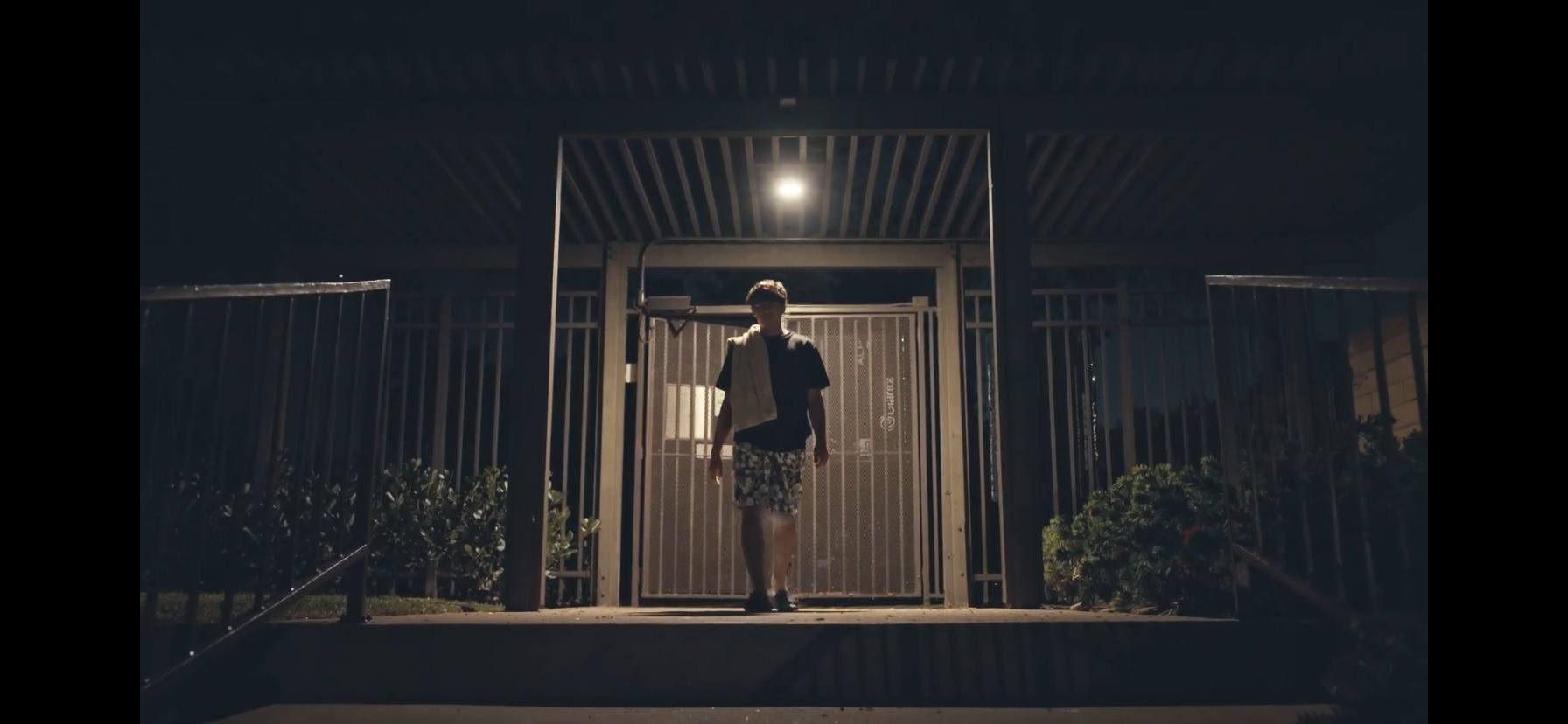 Person standing outside a gated entrance at night under a bright overhead light