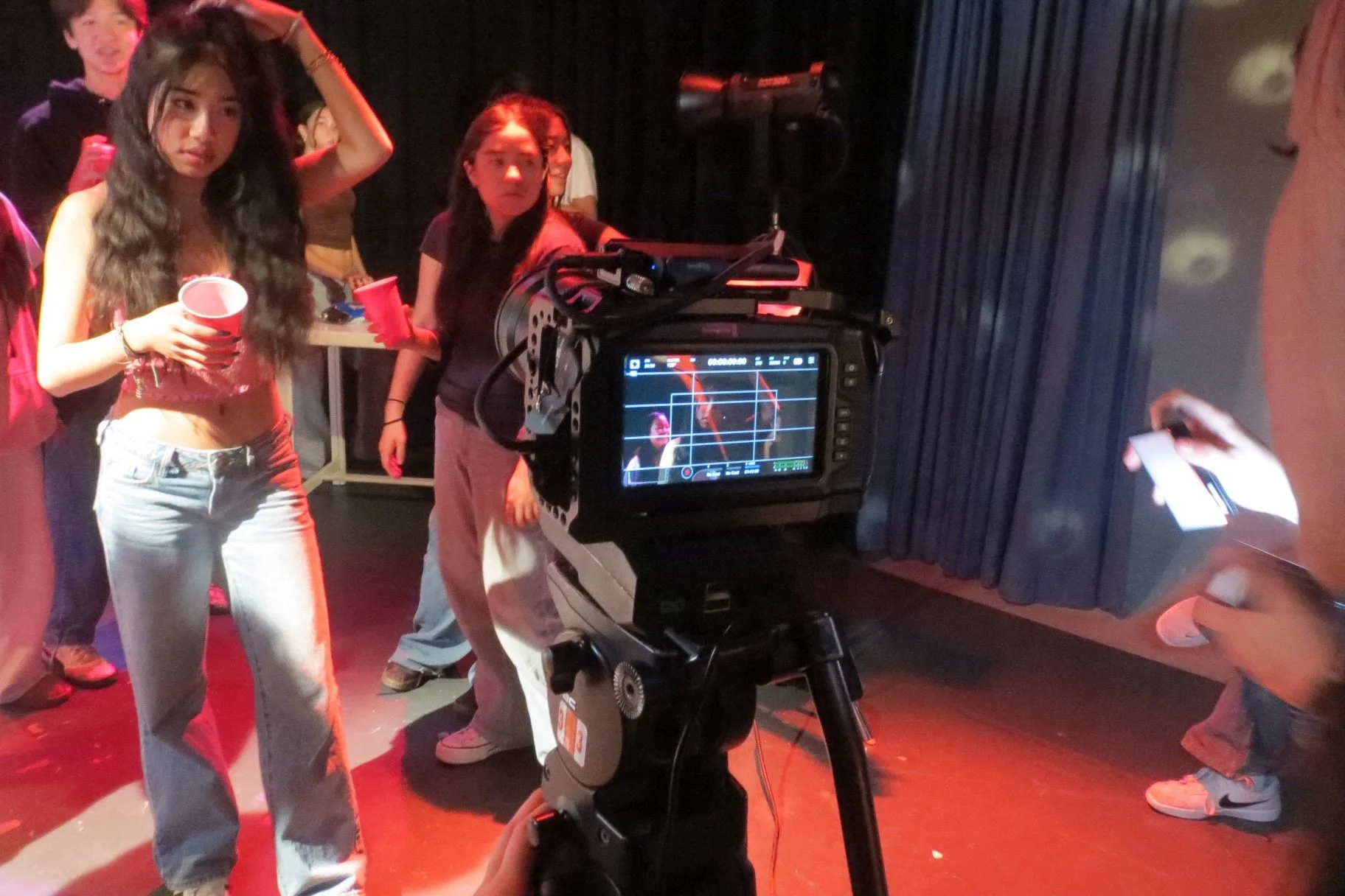 Film camera recording people backstage under red stage lighting