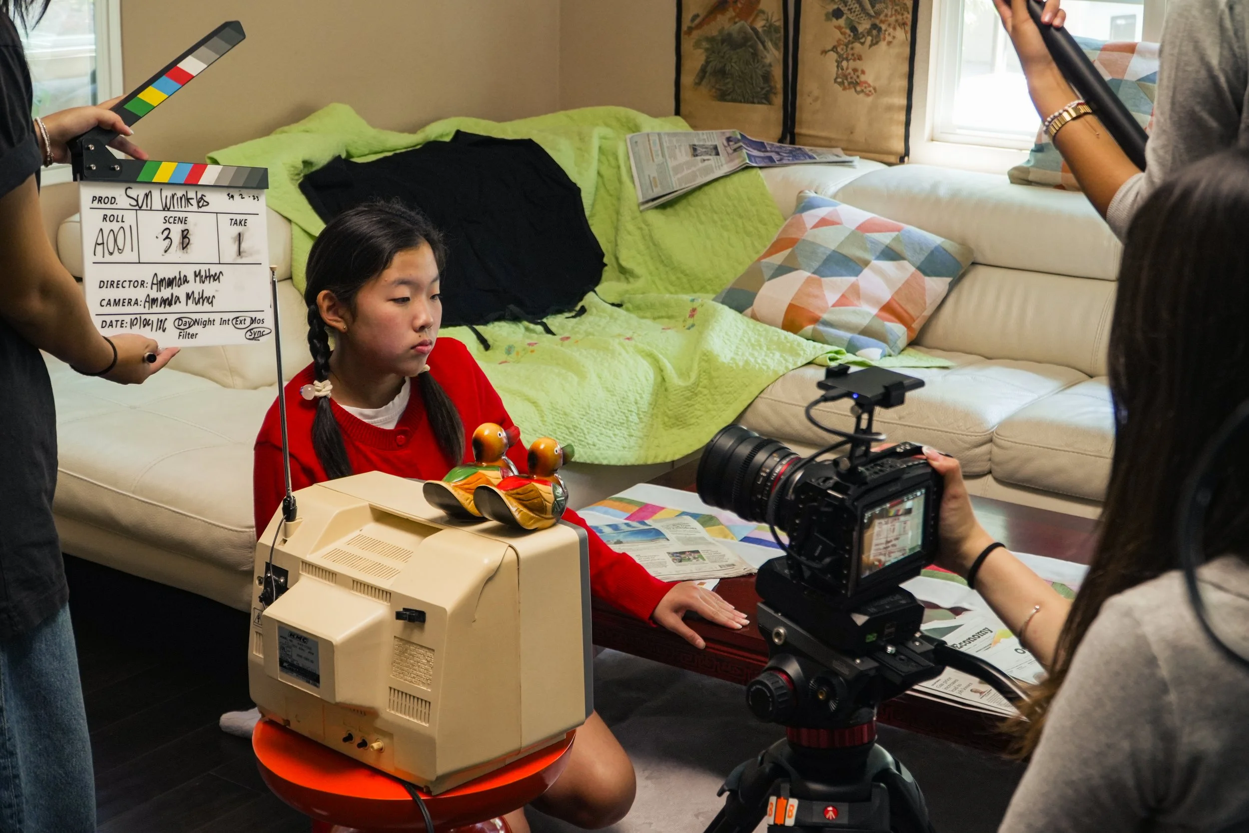 Film crew shooting a scene with a clapperboard, camera, and young girl in a living room