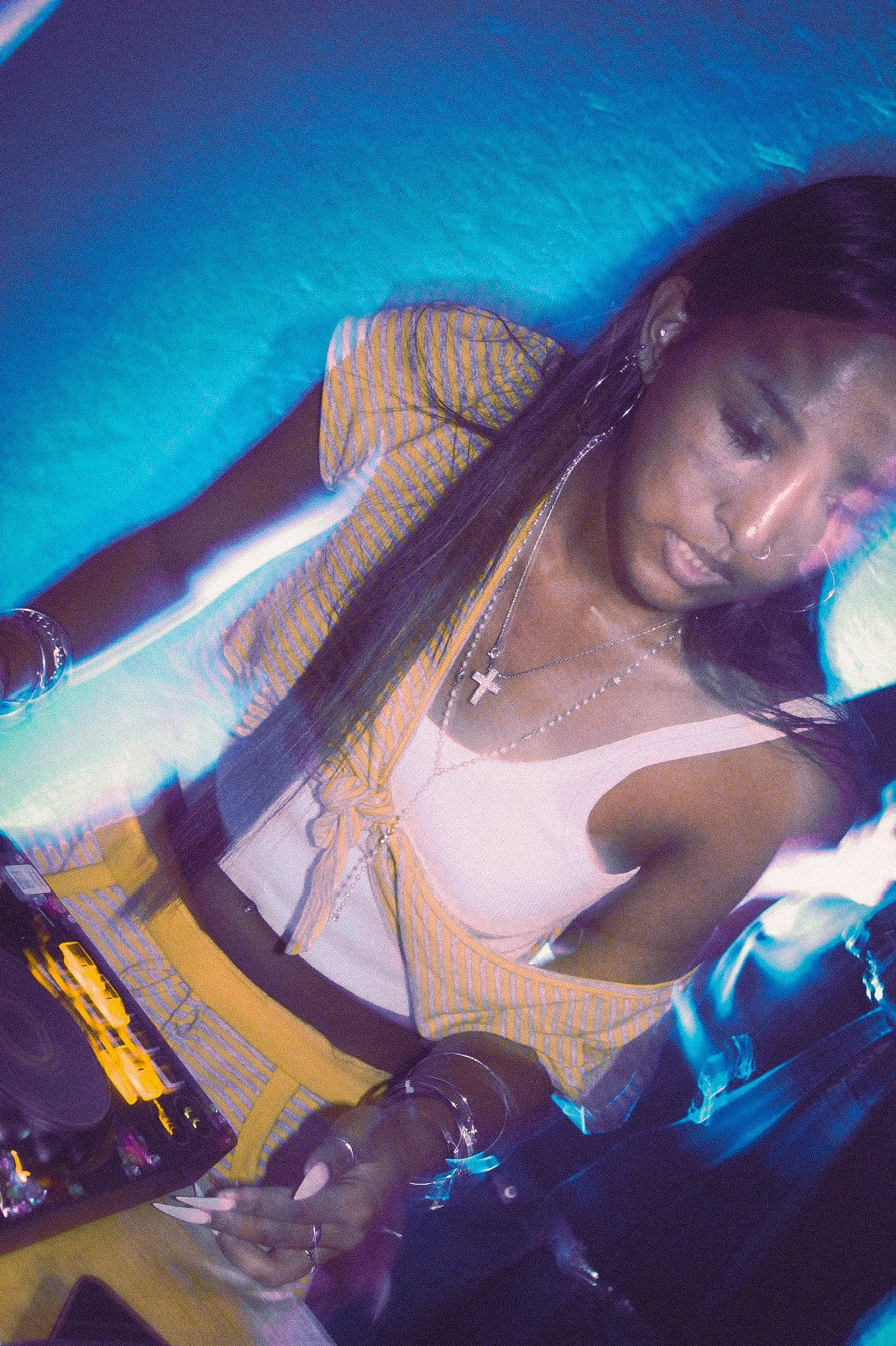 Person wearing sunglasses, a striped shirt, layered cross necklaces, and a headscarf at a colorful event