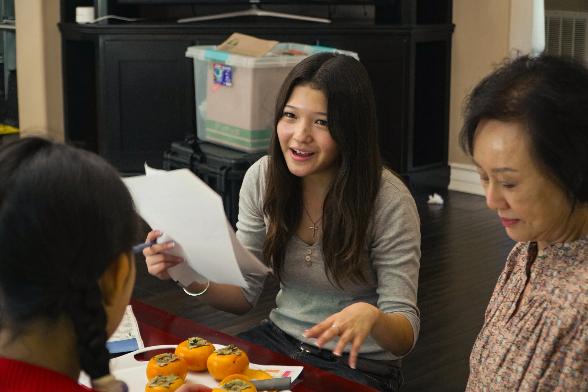 Group of people gathered around a table, discussing papers beside sliced persimmons.
