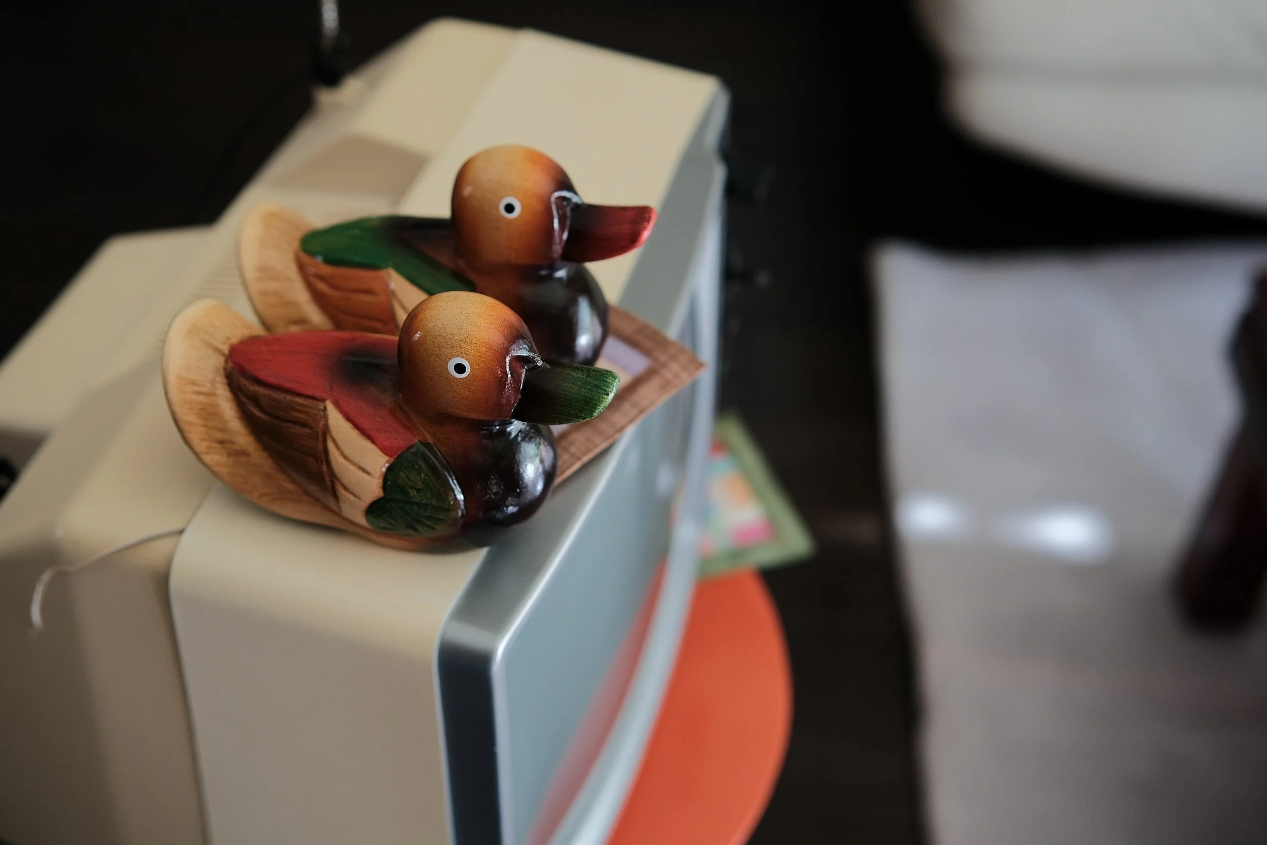 Two colorful wooden duck figurines on a small wooden tray beside a computer monitor