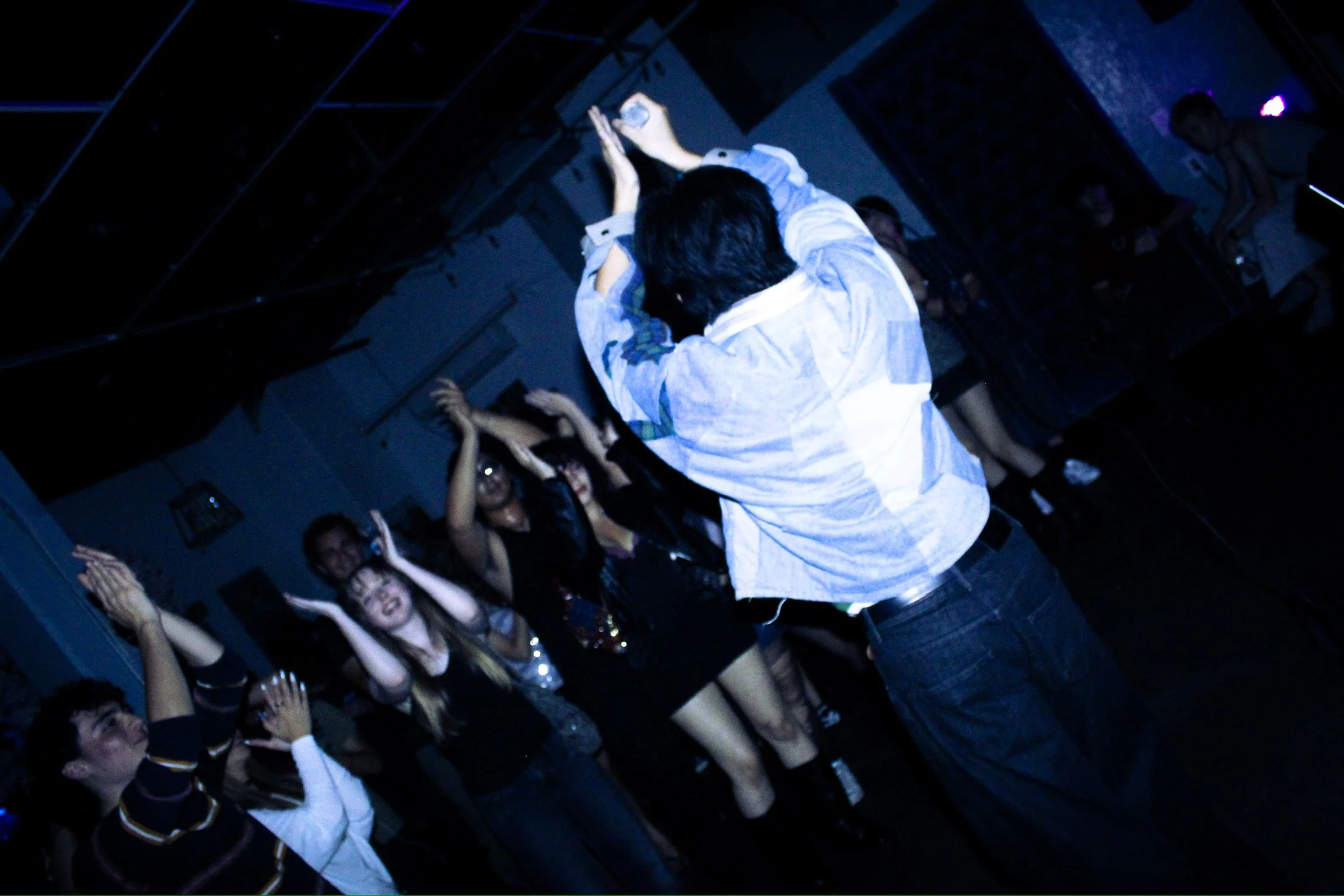 Singer in a white shirt reaching toward an enthusiastic concert crowd under blue stage lighting