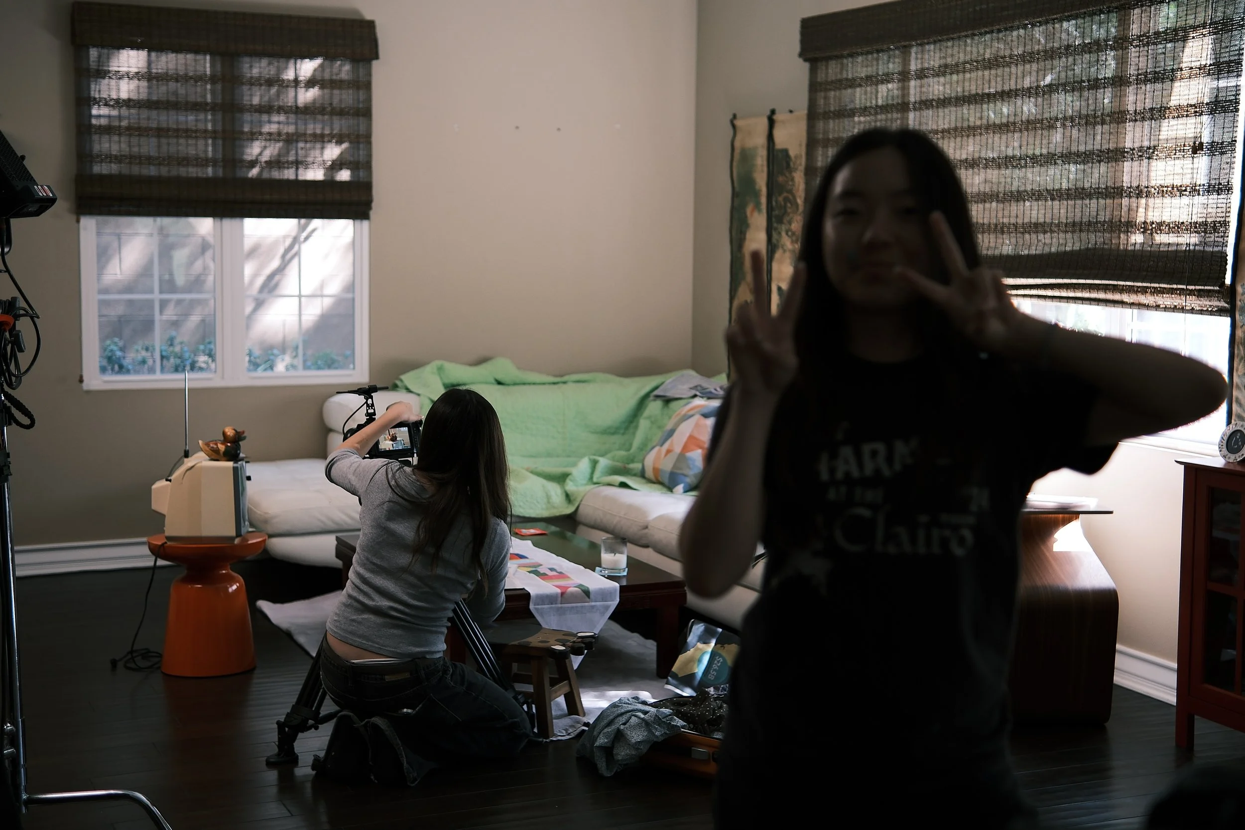 Person posing in front of a camera while another person films in a living room