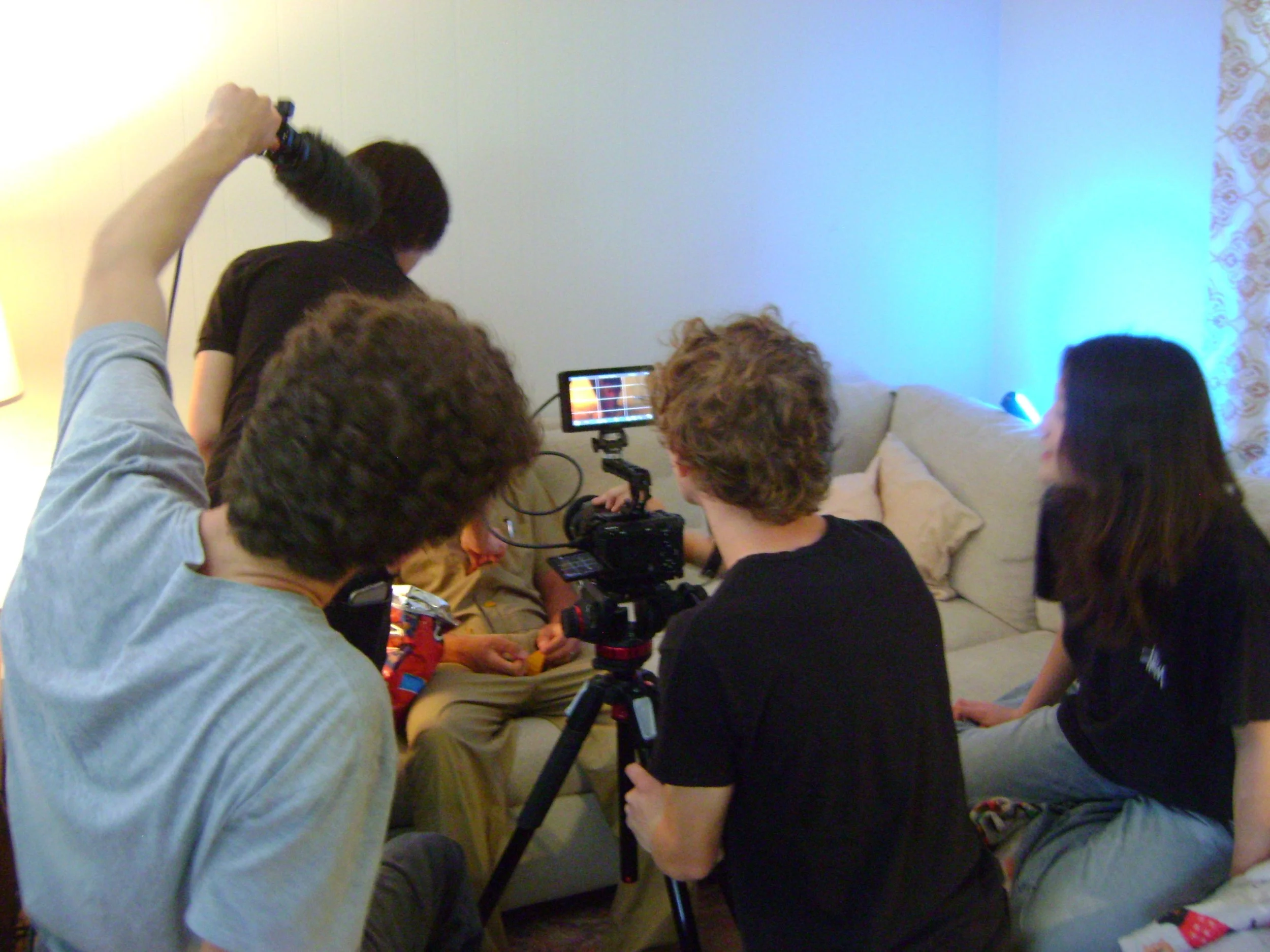 Film crew recording a scene indoors with a camera, monitor, and boom microphone.