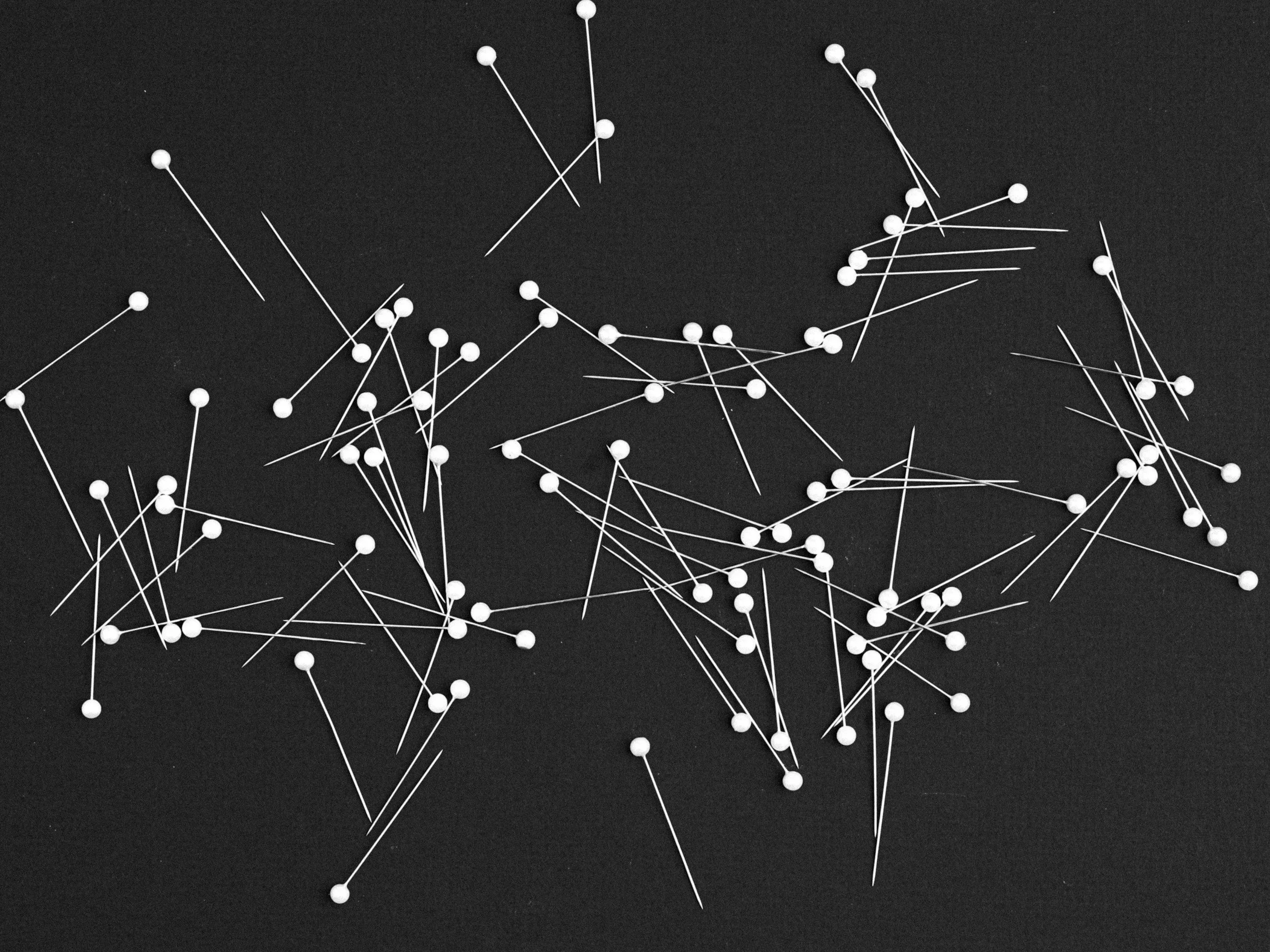 Numerous white sewing pins scattered on a black surface.