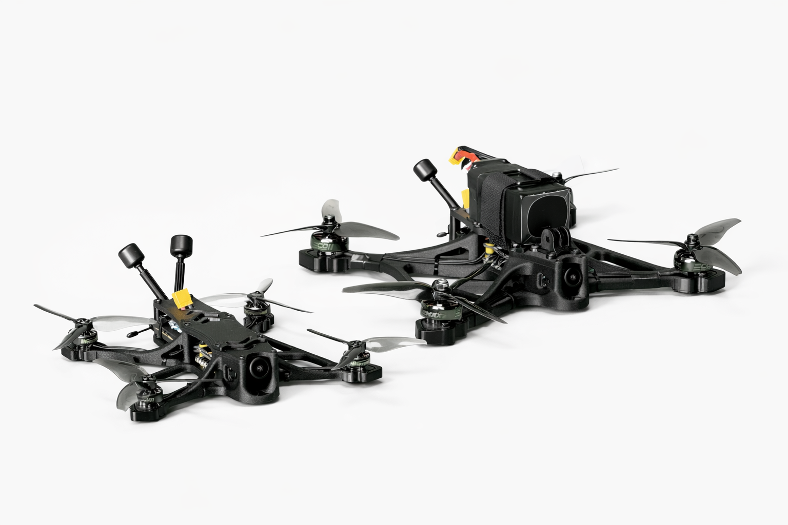 Two black racing drones with camera mounts and four propellers each on a white background.