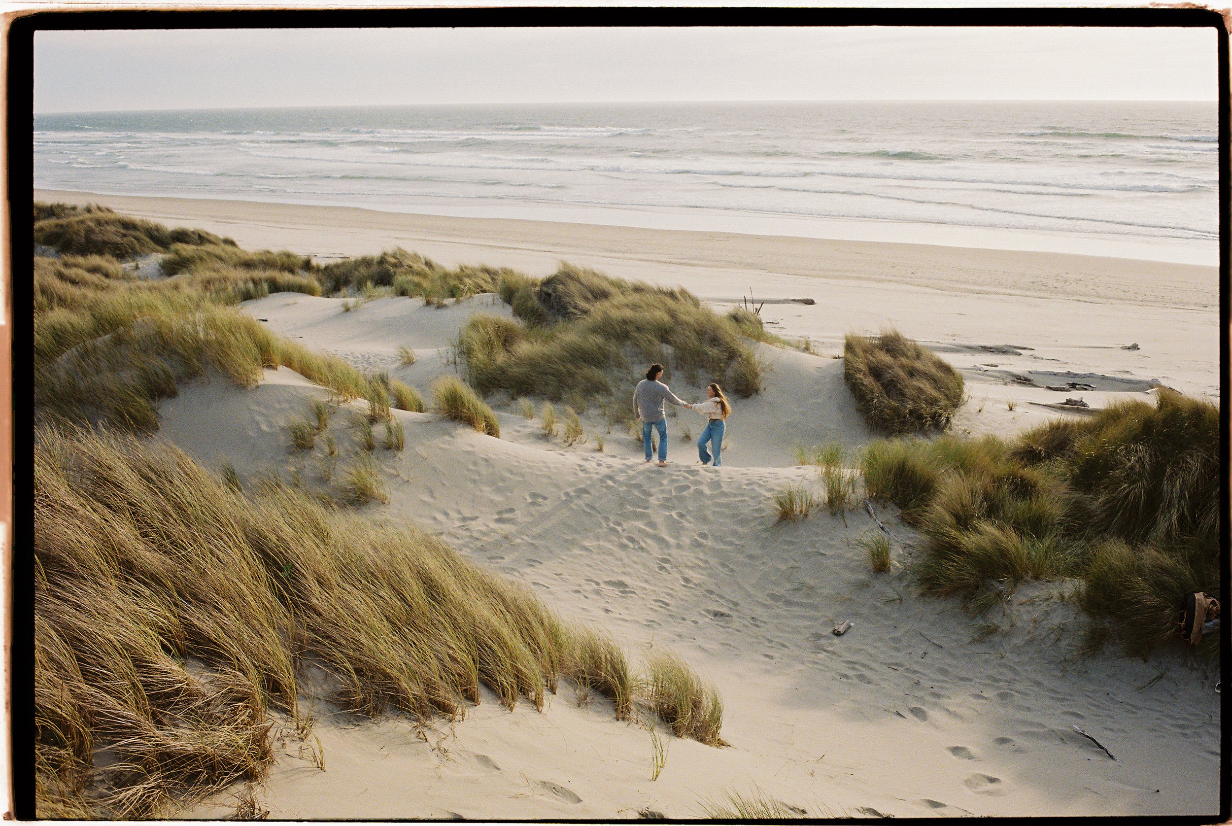 engagement photos of a bride and groom holding hands on a sand dune on the oregon coast
