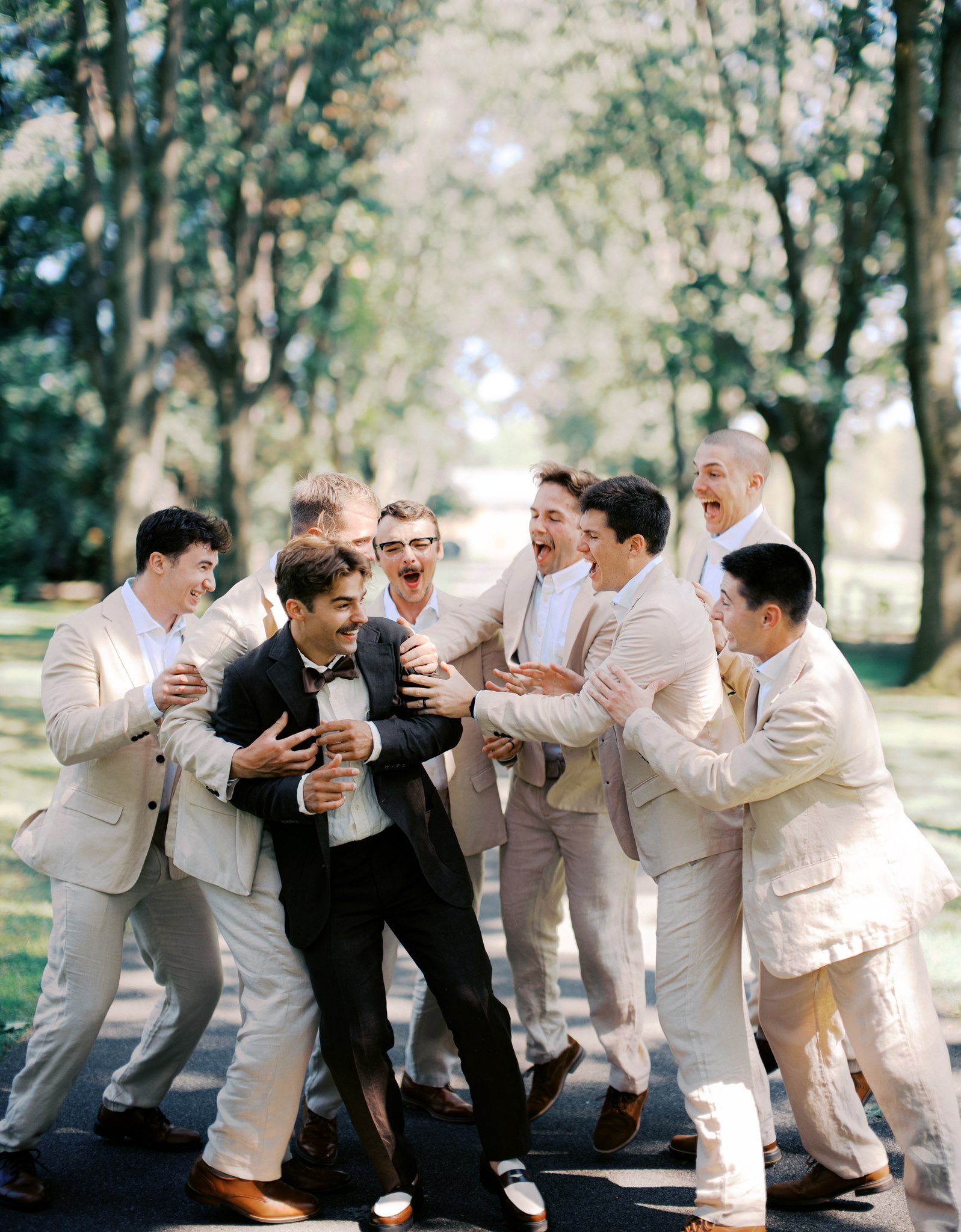 groom and groomsmen all gathered around each other laughing and horseplaying