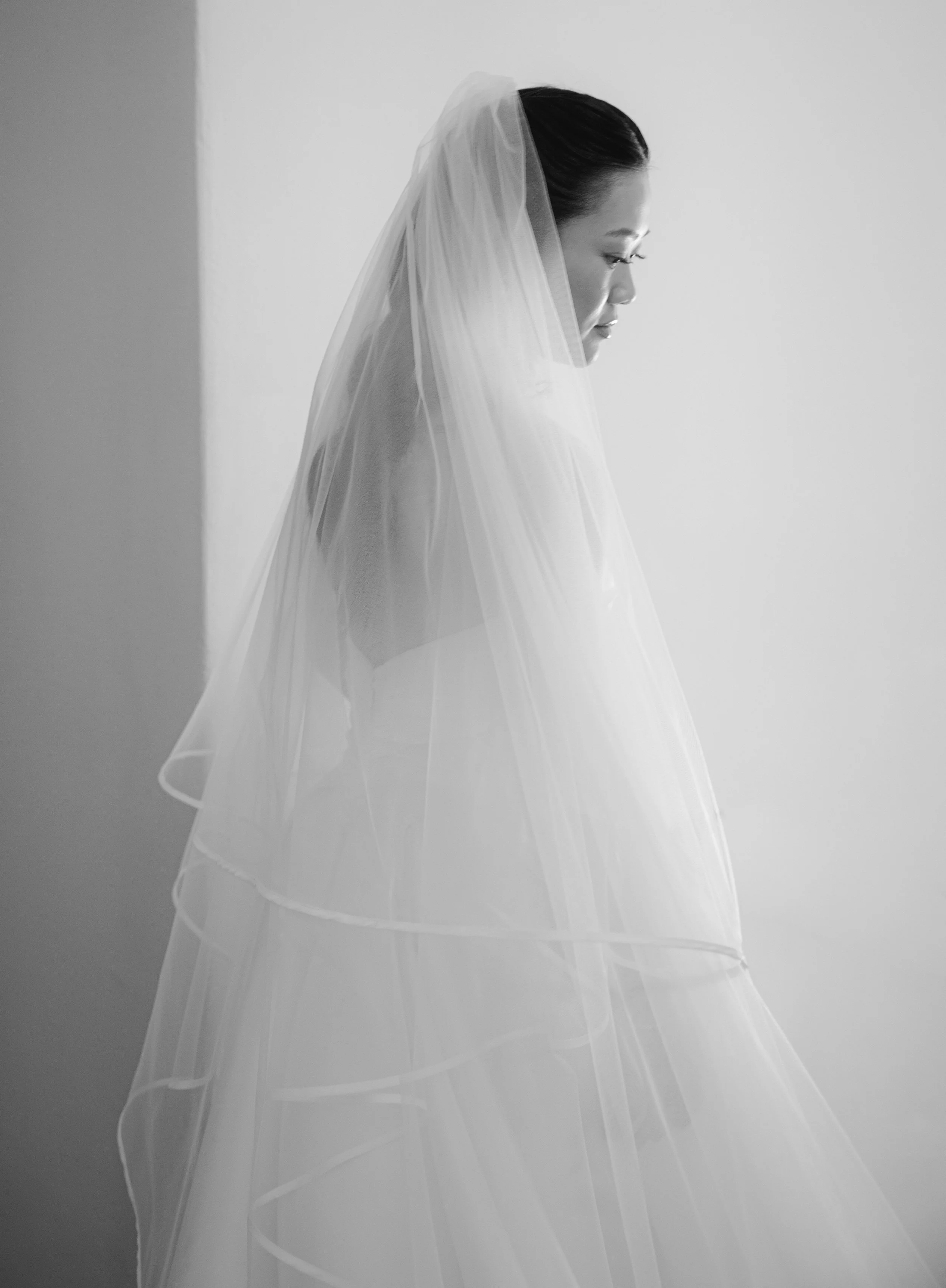 Black and white side profile of a woman wearing a veil, with a neutral background.