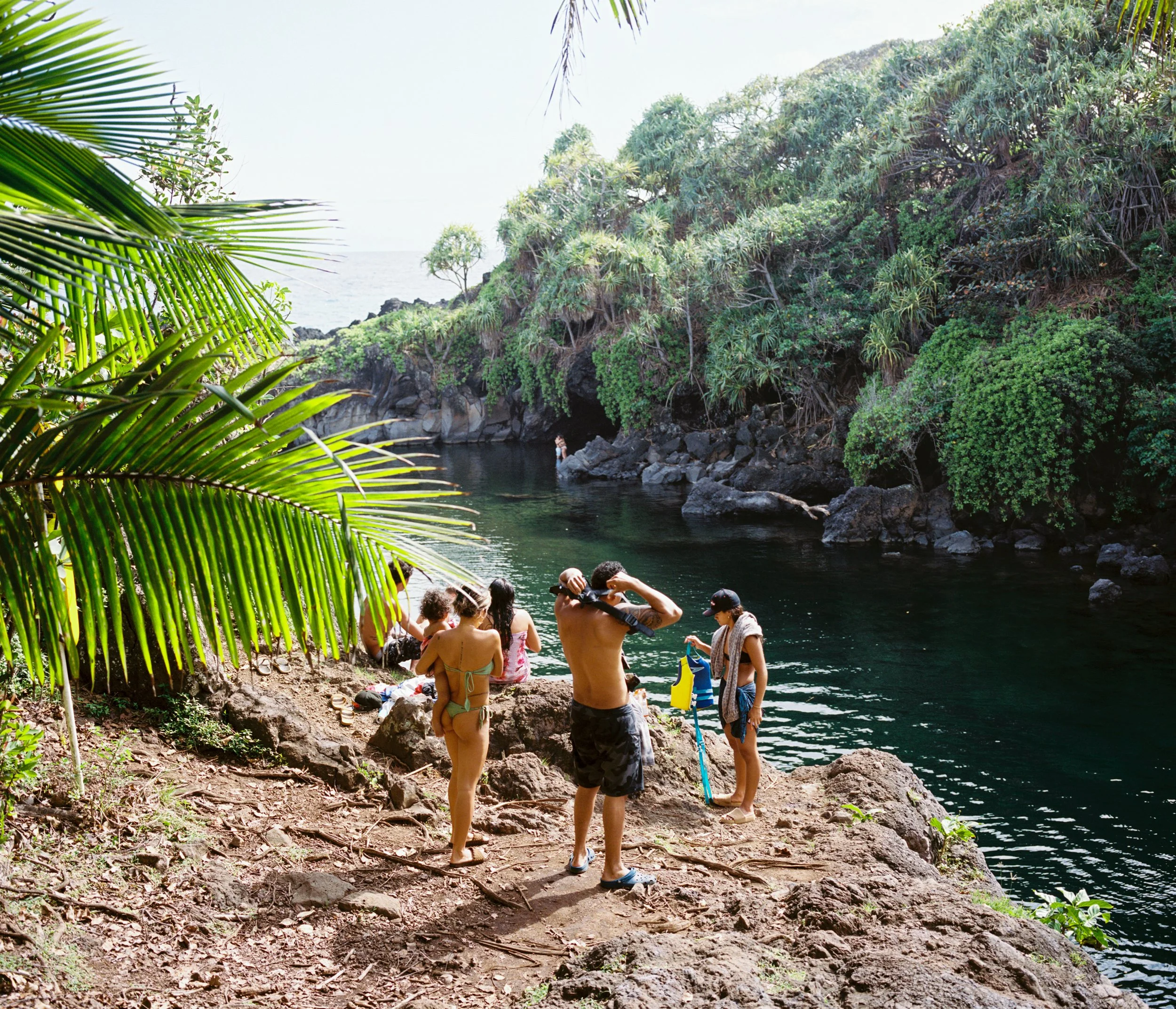 People relaxing by a river in a tropical area with lush green vegetation and rocky banks.