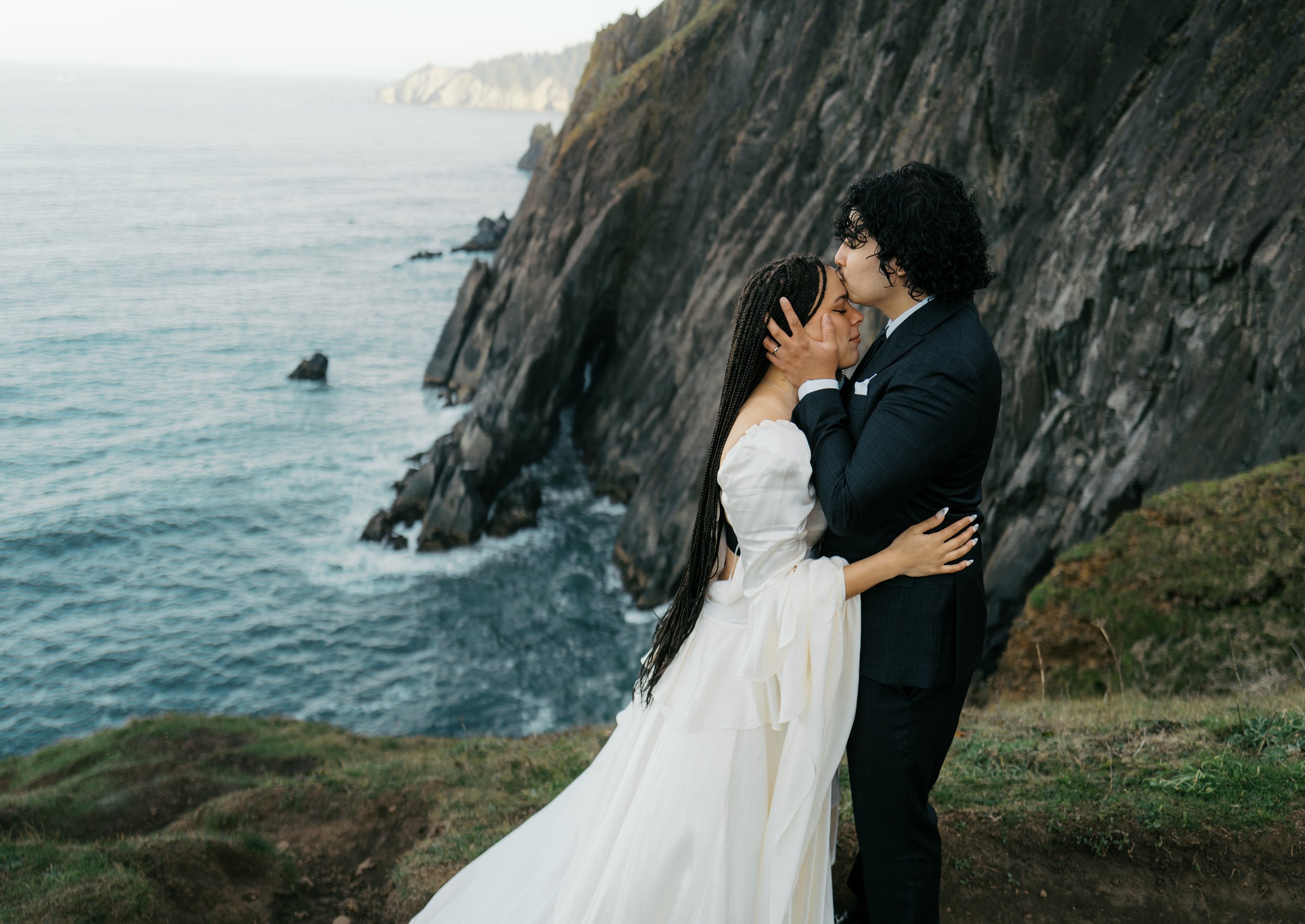 a groom kissing a bride on the edge of a cliff on the oregon coast