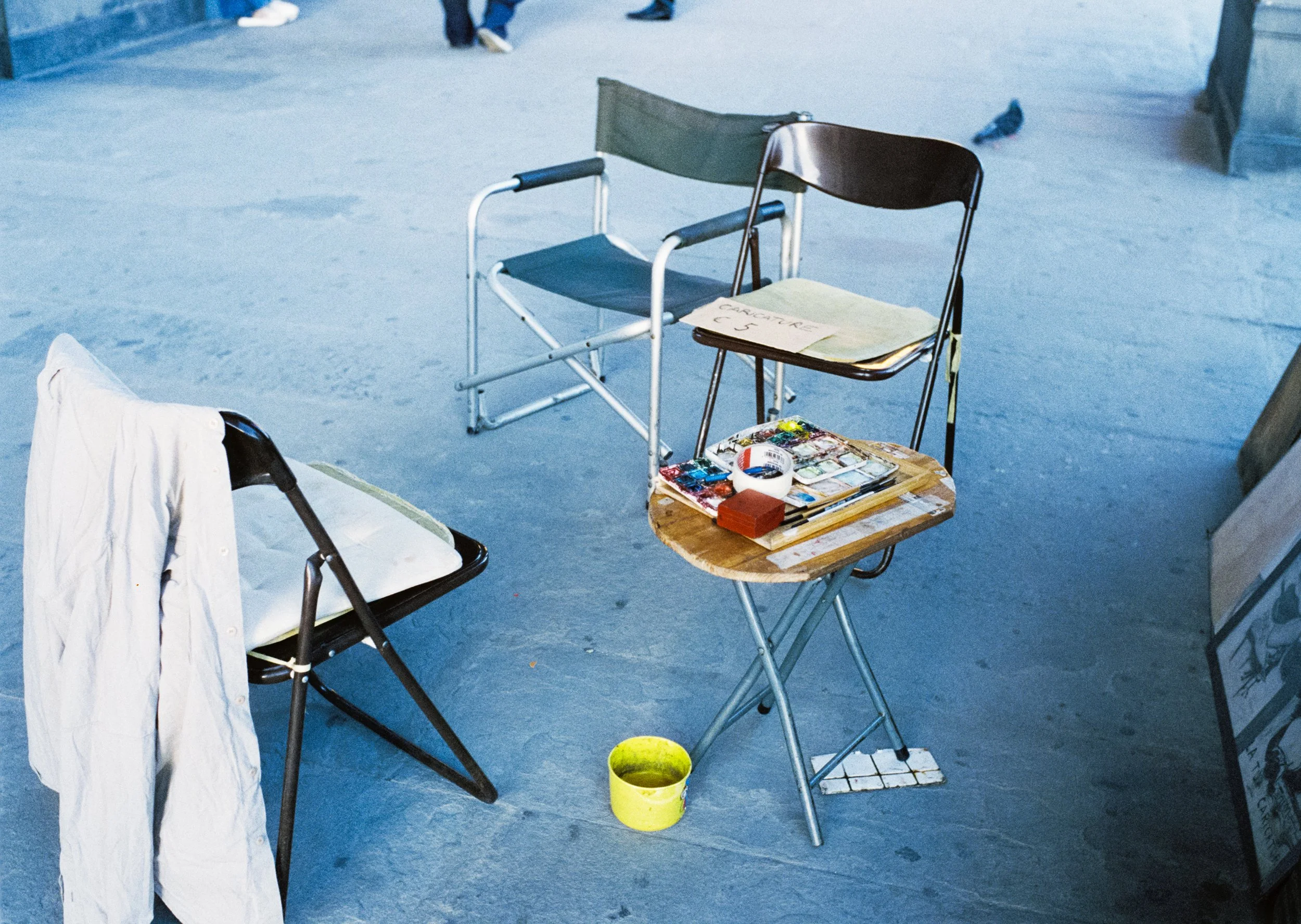 Empty outdoor seating area with chairs and a small wooden table with art supplies on it, painted concrete ground.