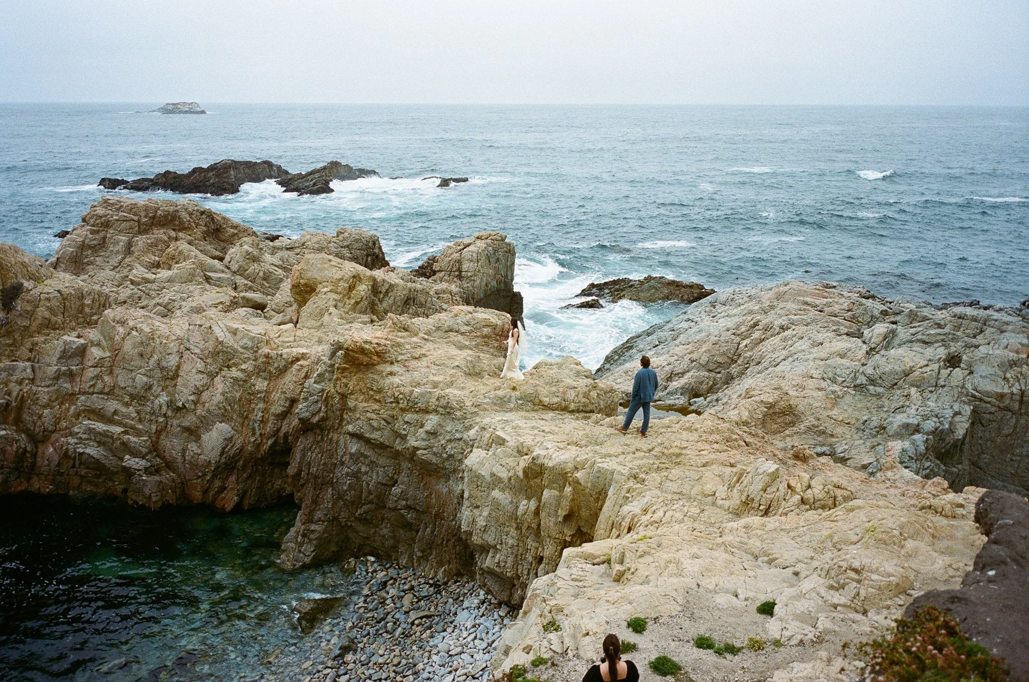 the bride and groom standing on the cliffs of big sur on film