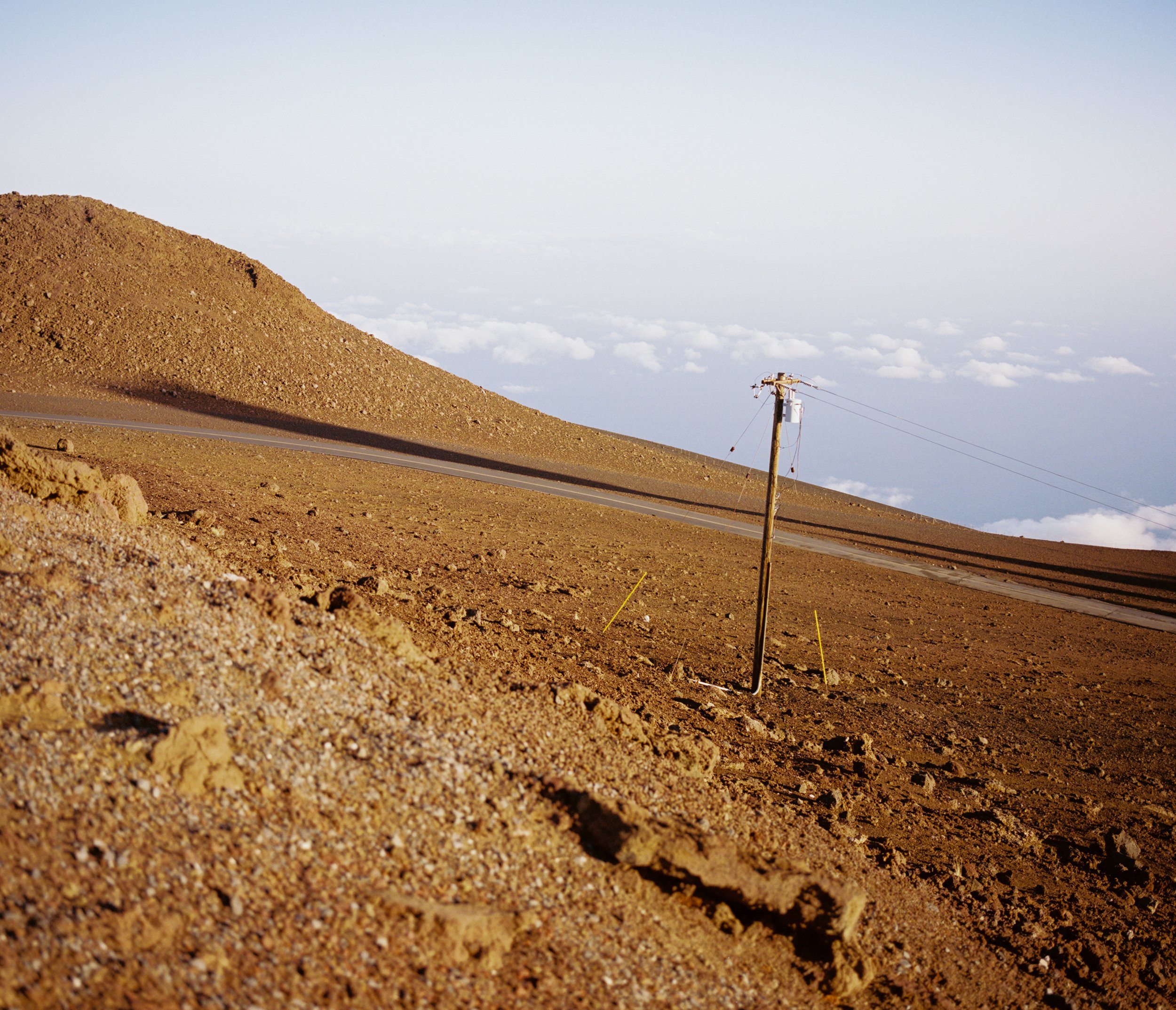 A dirt road on a barren hill with a utility pole, under a partly cloudy sky.