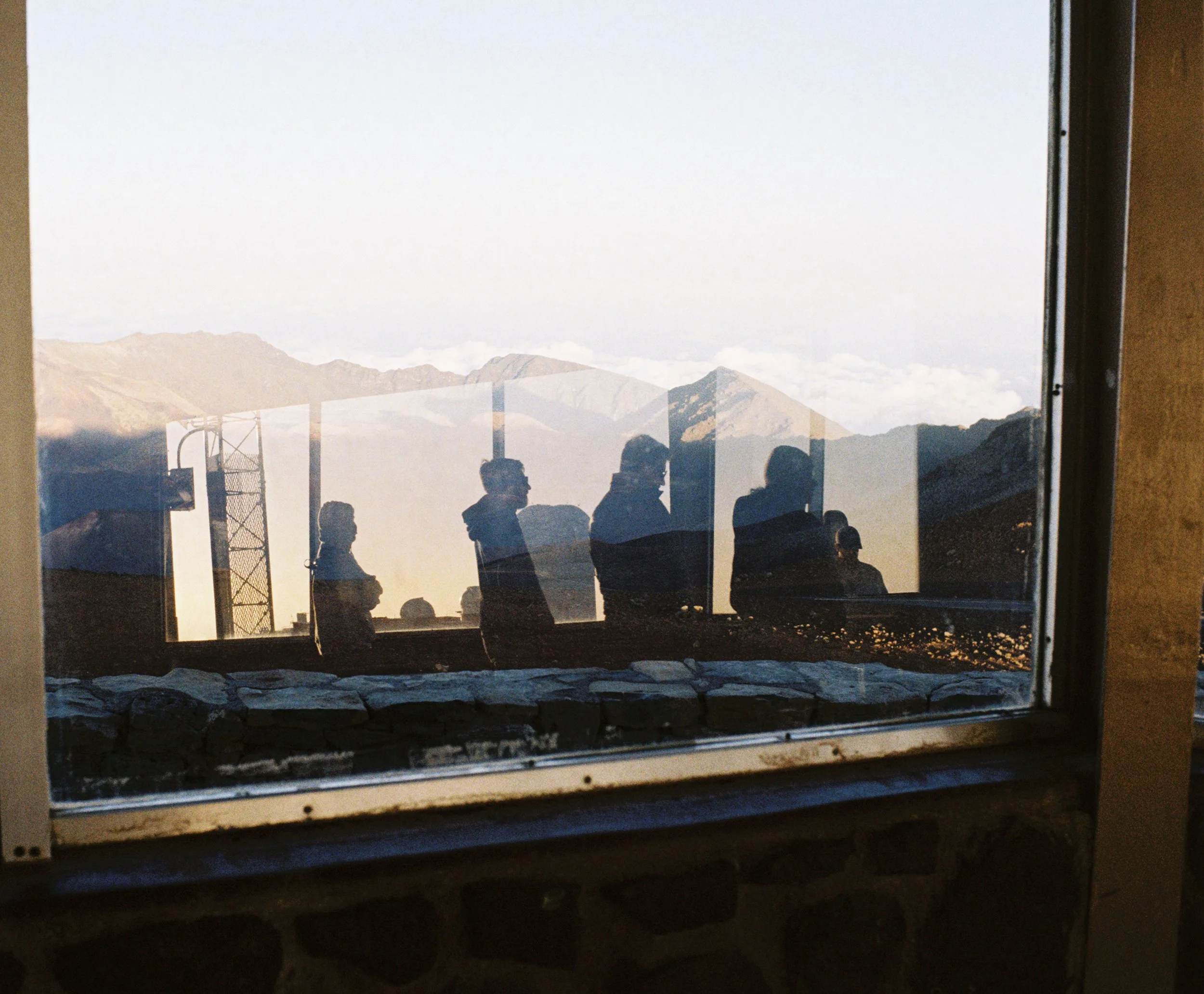 Reflection of people and mountains seen through a window with a rainbow display, with a mountain landscape in the background.