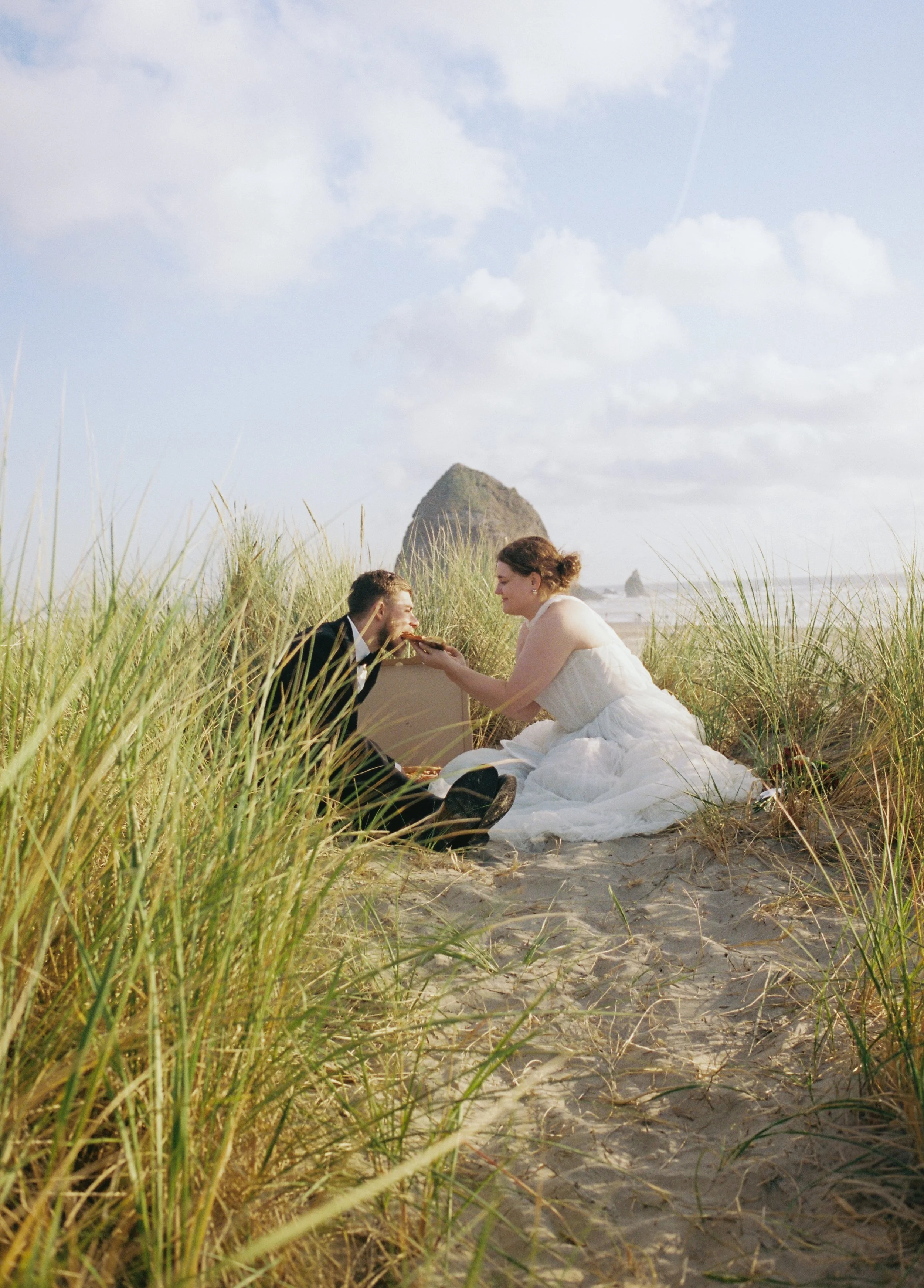 film of a bride feeding the groom pizza near haystack rock on cannon beach