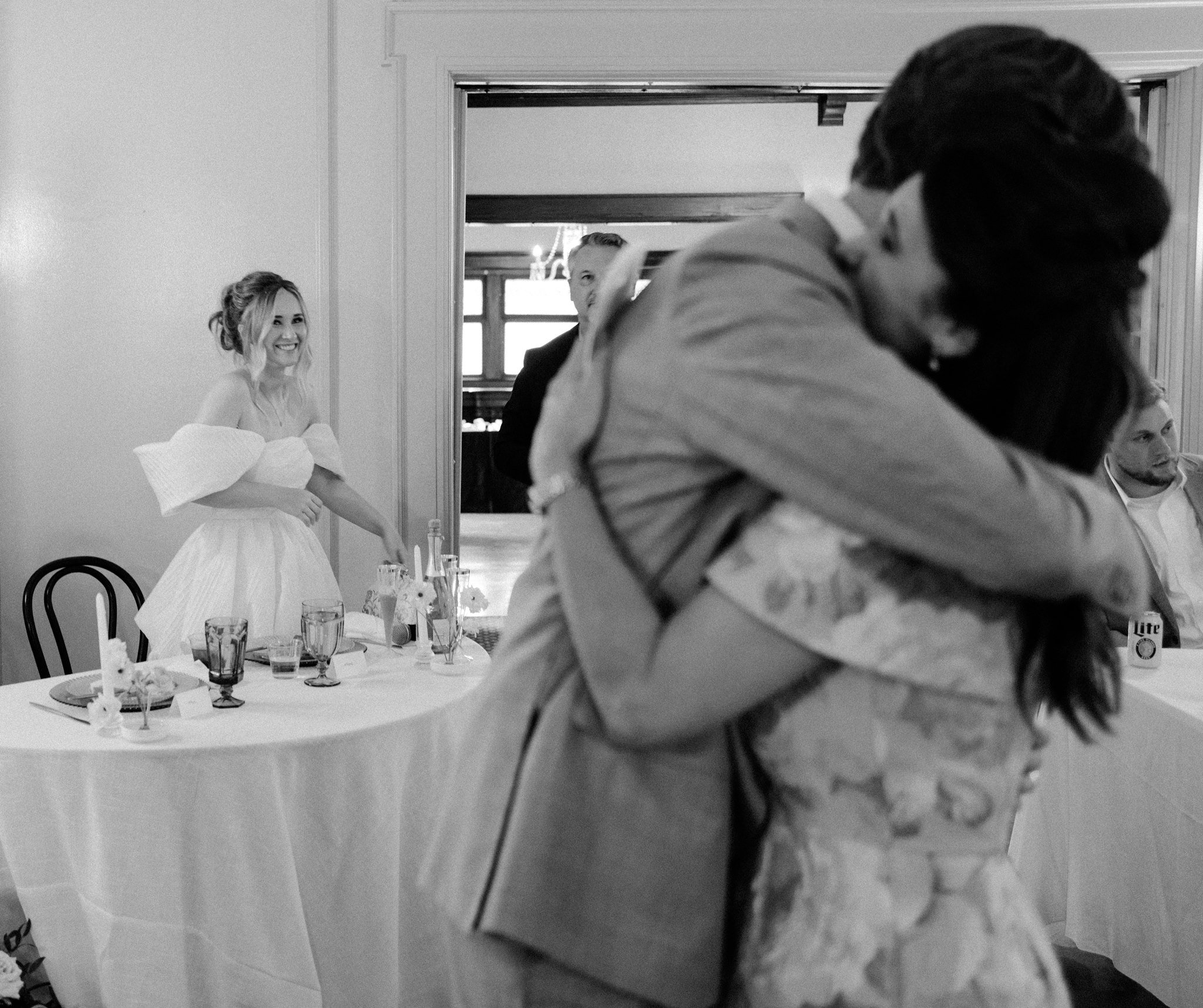 a bride watching the groom hug his mother after after wedding speeches