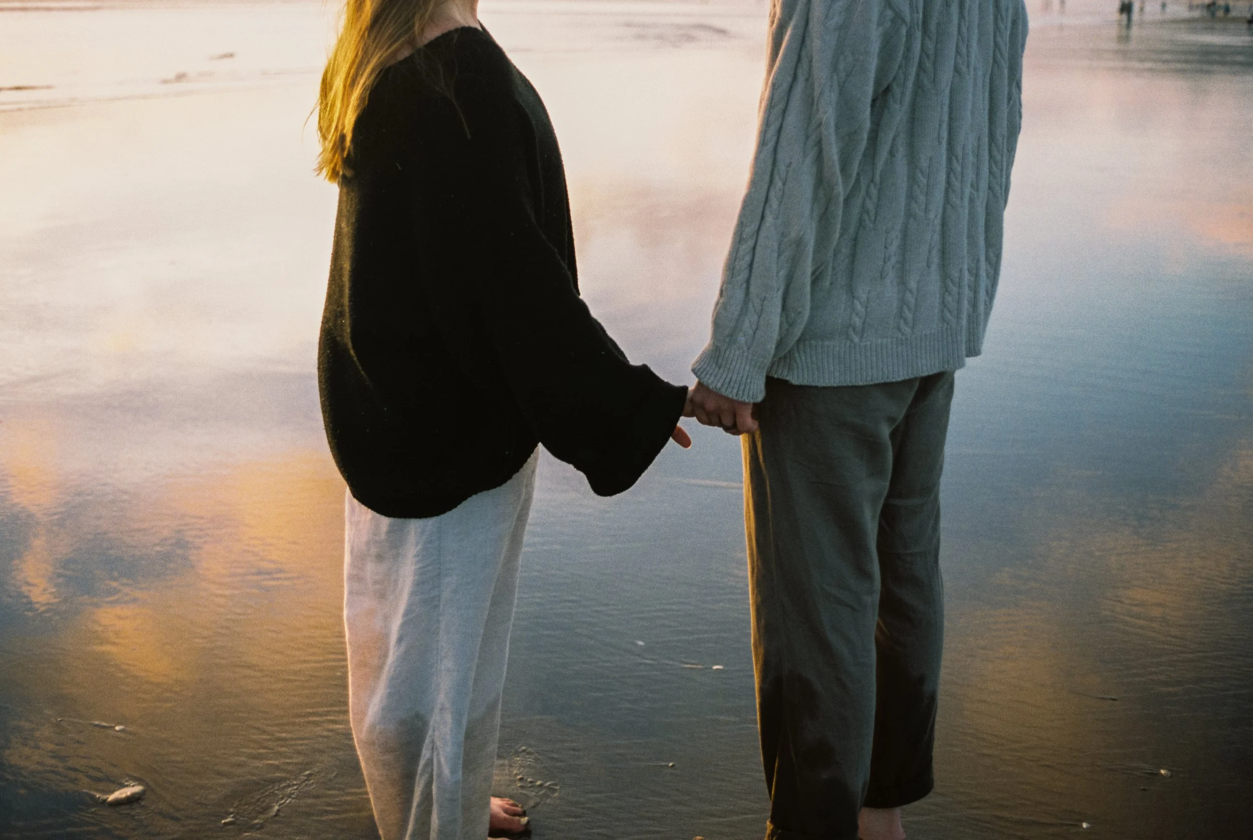a couple holding hands with the reflection of a sunset in the ocean behind it