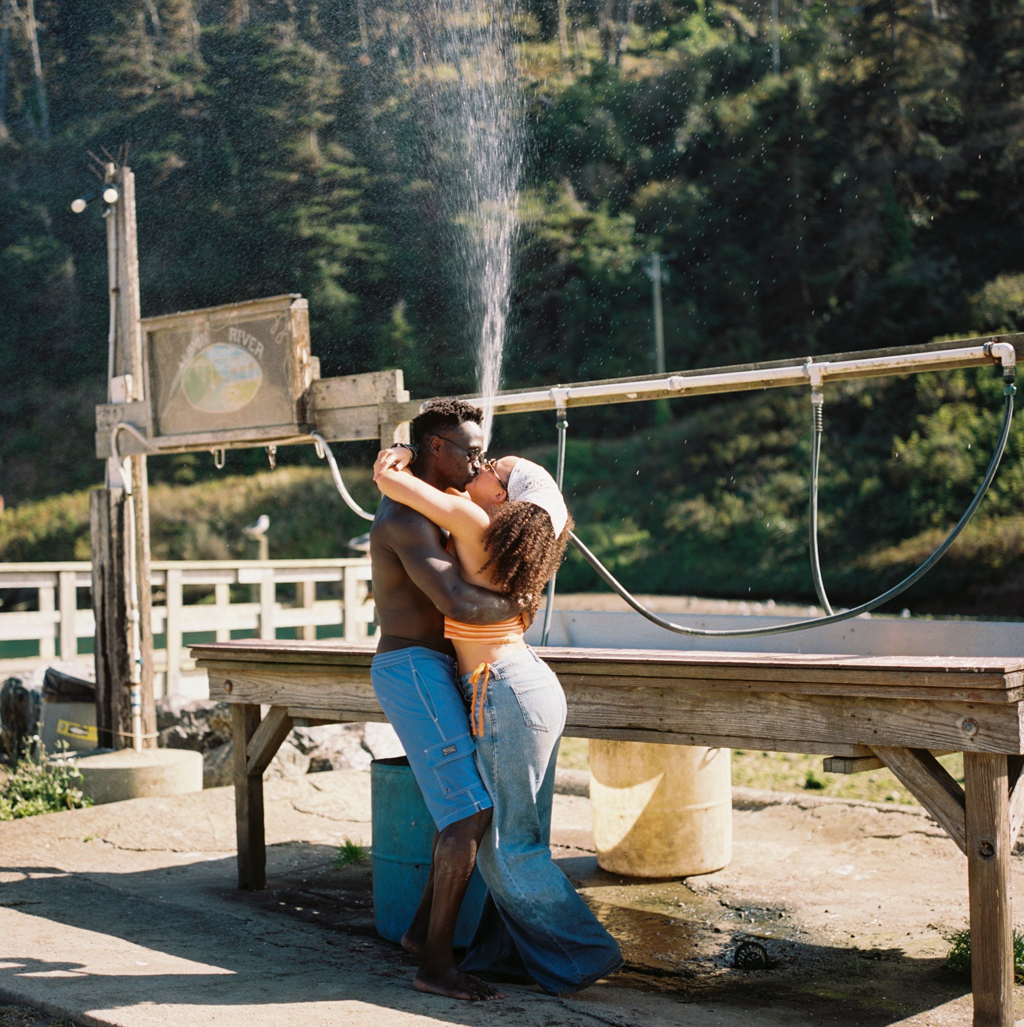 a couple under a sprinkler laughing and kissing on the california coast