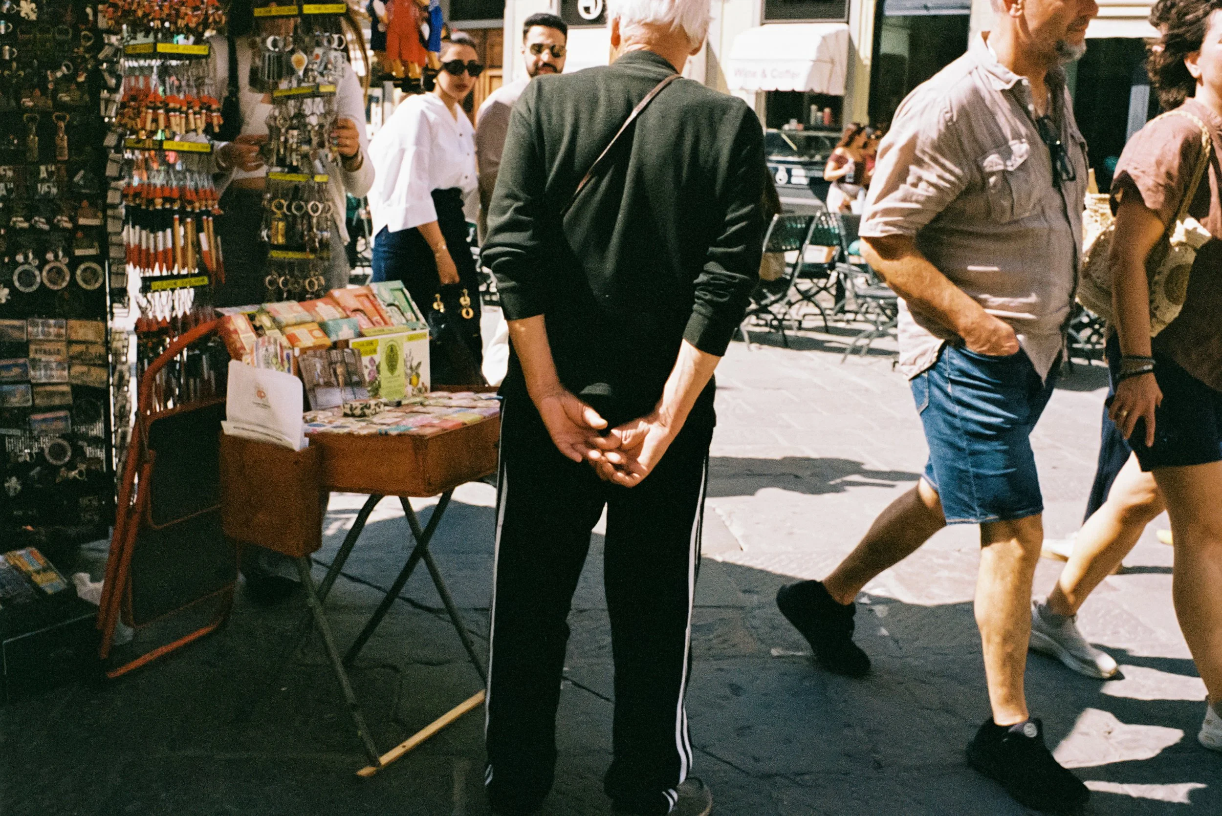 People walking past a street vendor selling items like souvenirs and accessories on a sidewalk in daytime.