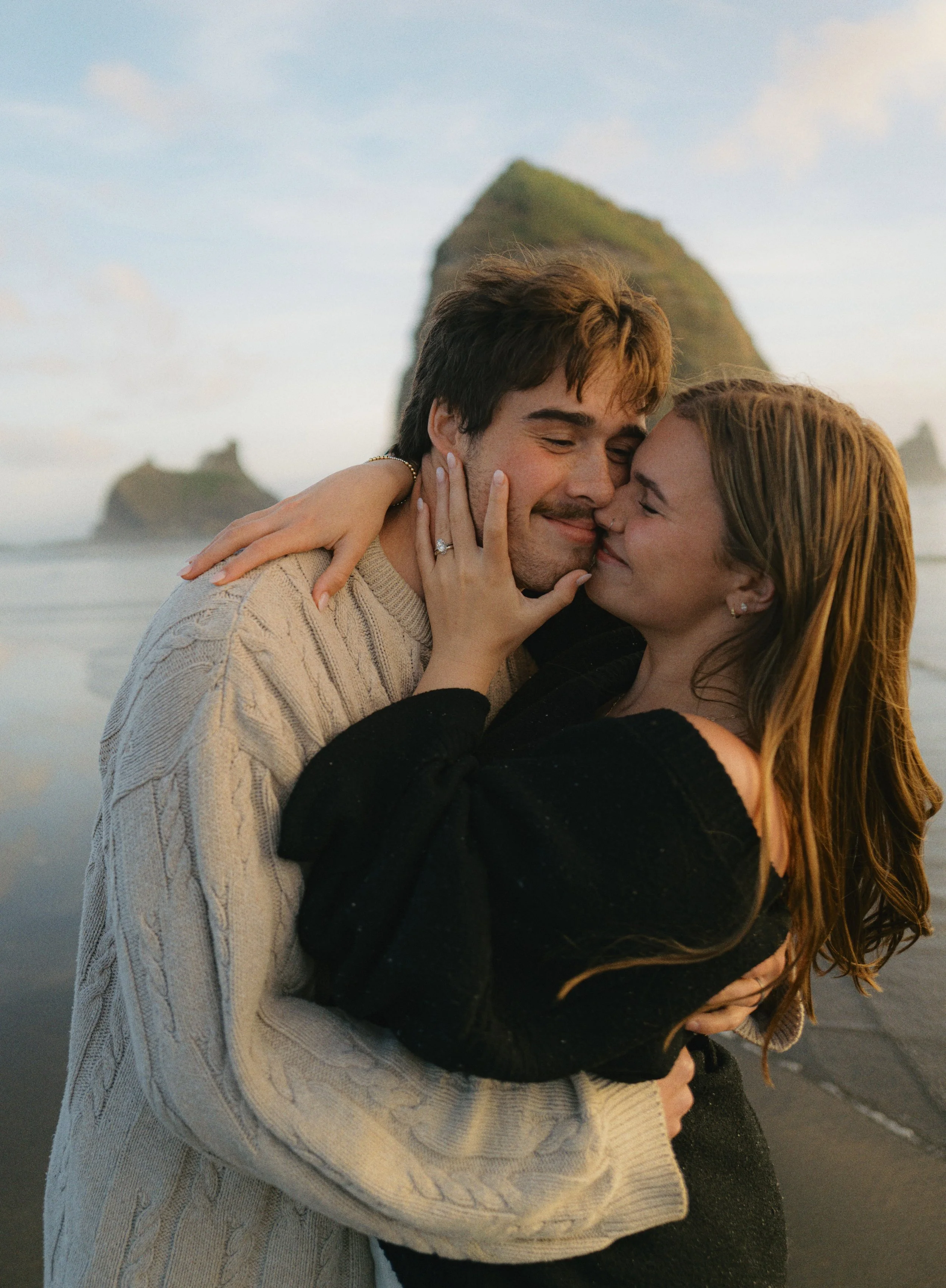 a couple kissing each other with Haystack Rock in Cannon Beach behind them
