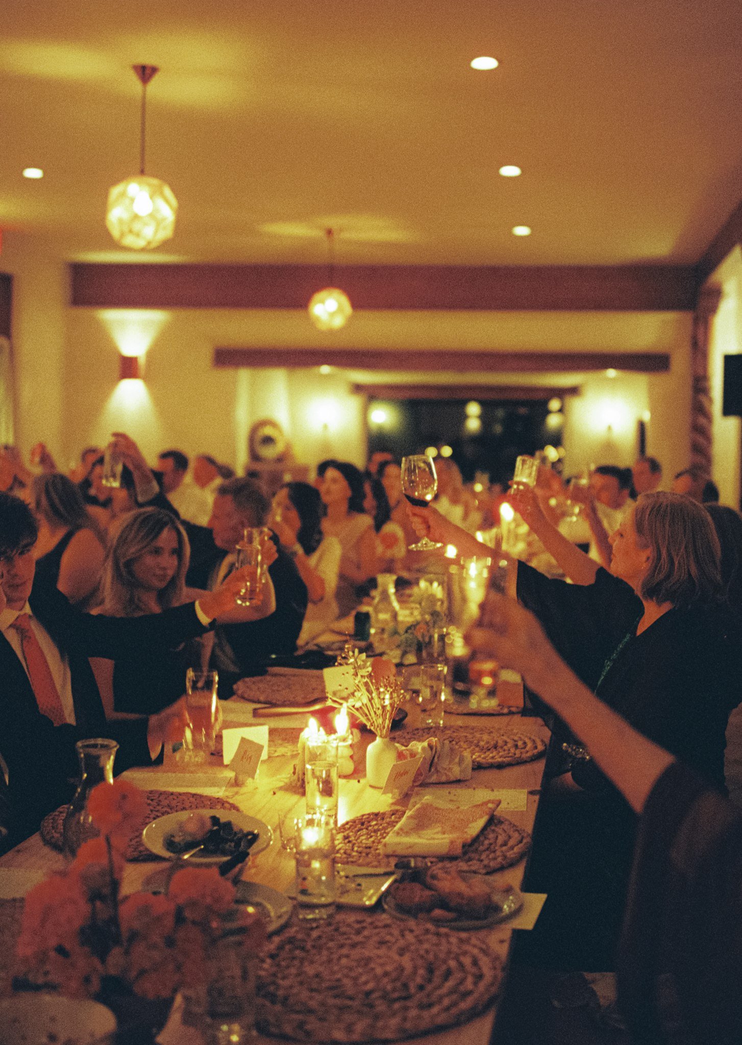 a film shot of guests raising their glasses to the bride and groom in warm lighting