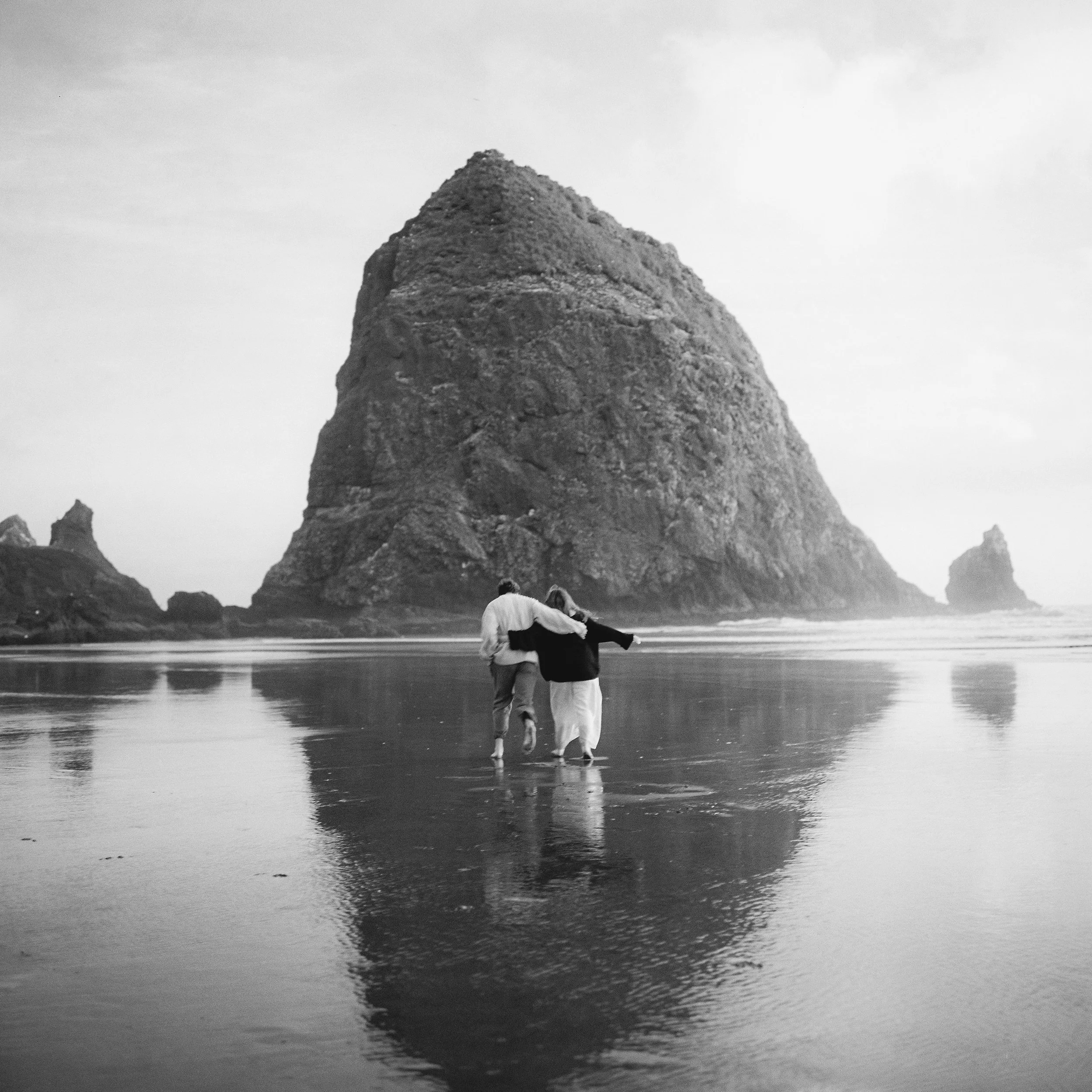 boy and girl running towards a sea stack rock in the ocean holding hands