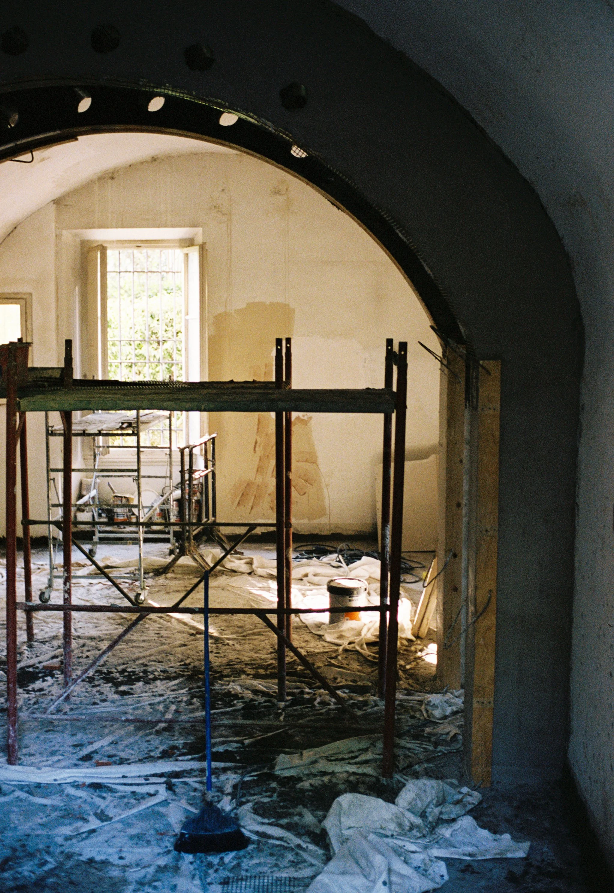 Room under renovation with scaffolding, construction tools, and materials, natural light coming through open window.
