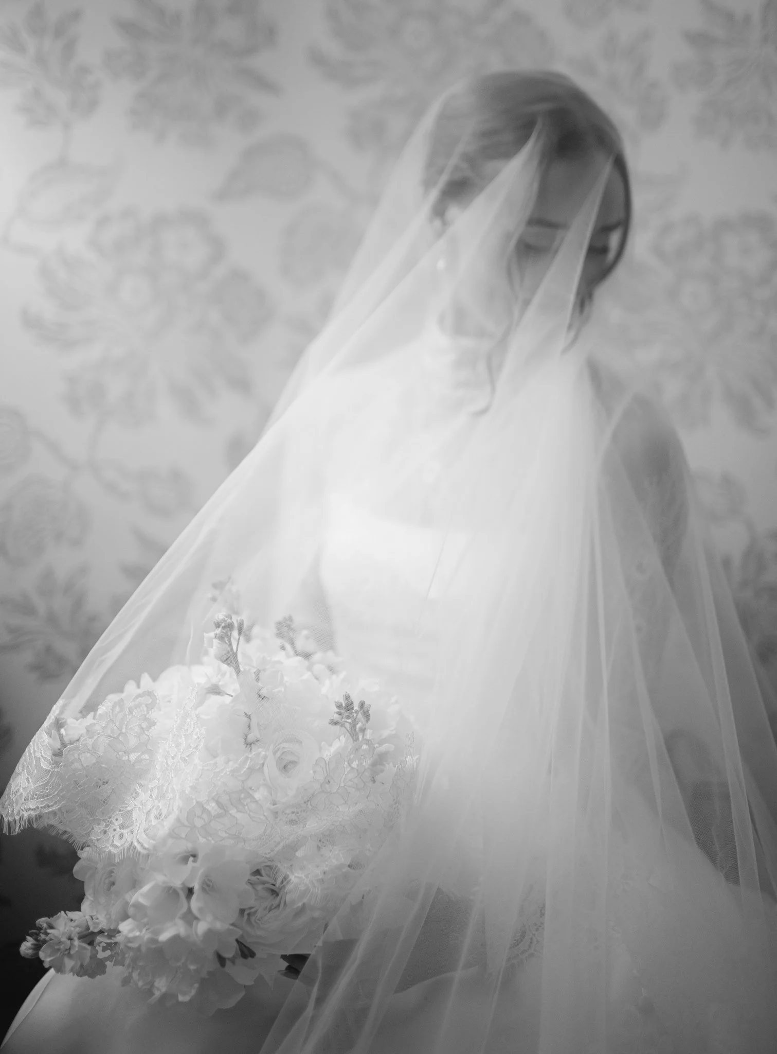 A woman dressed in a white wedding gown with a veil and holding a bouquet of flowers.