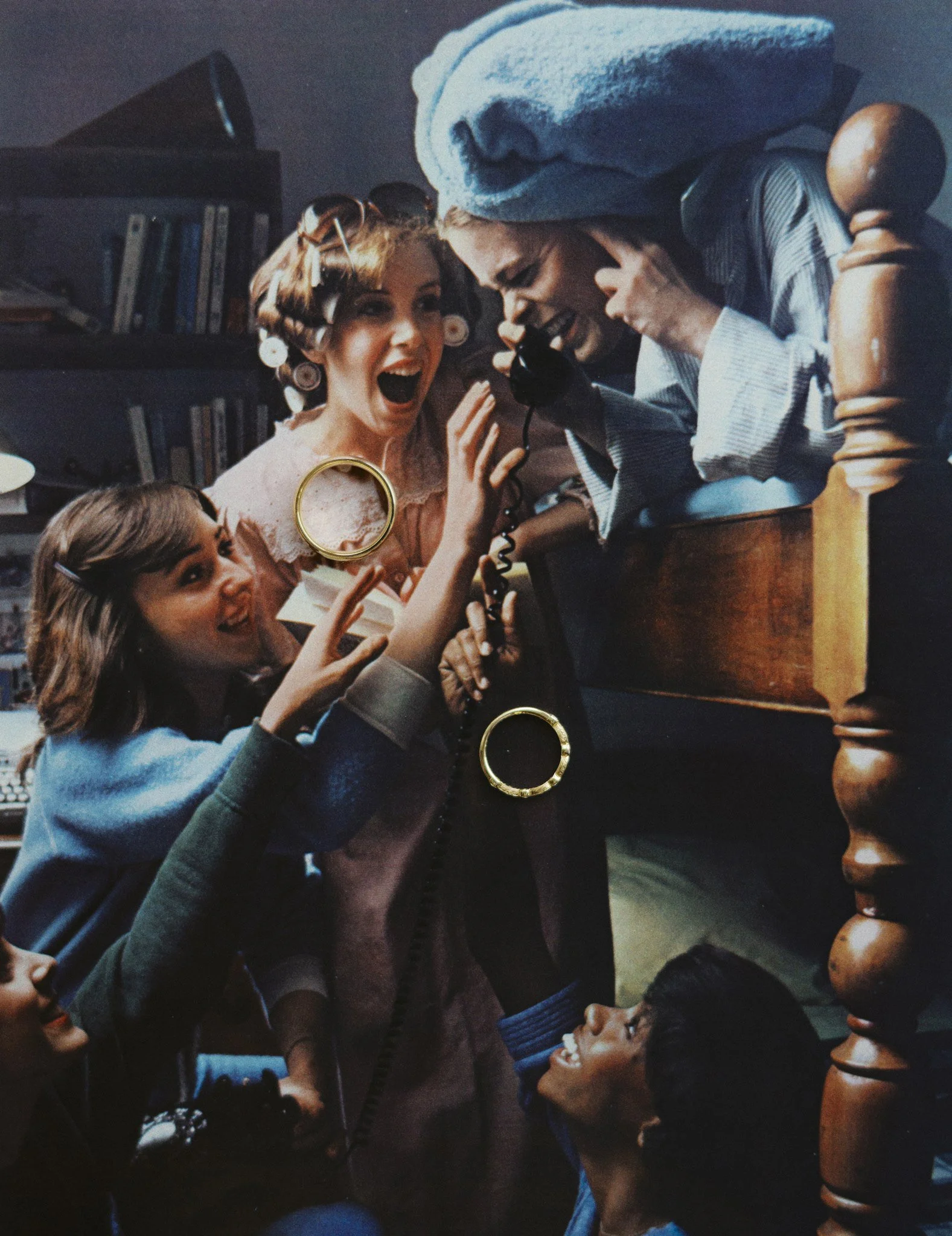 A woman with curlers in her hair and a woman with hair in rollers talk on a vintage telephone, smiling and laughing, in a cozy living room with a bookshelf in the background.