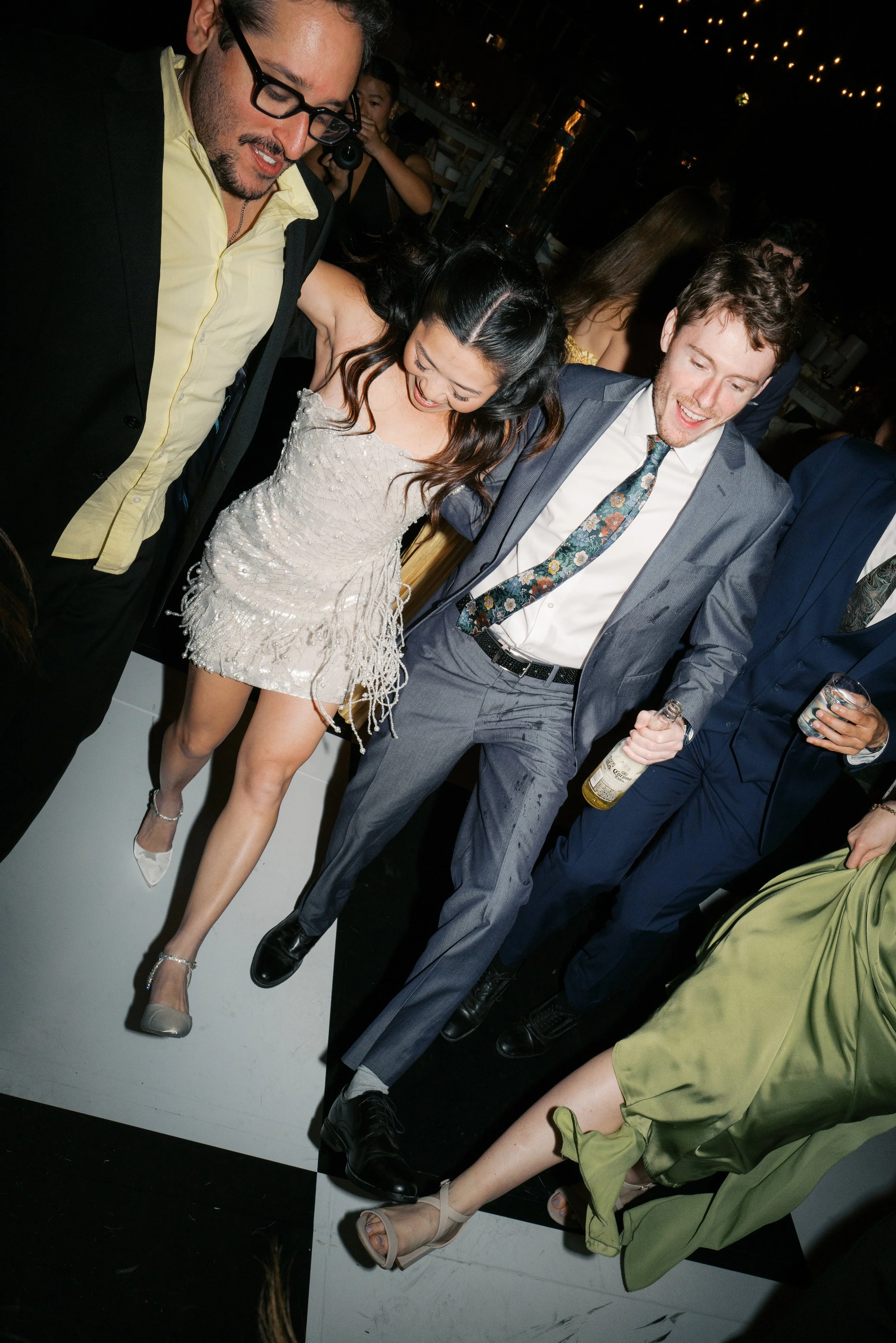 People dancing at a party, with a woman in a white dress and men in suits