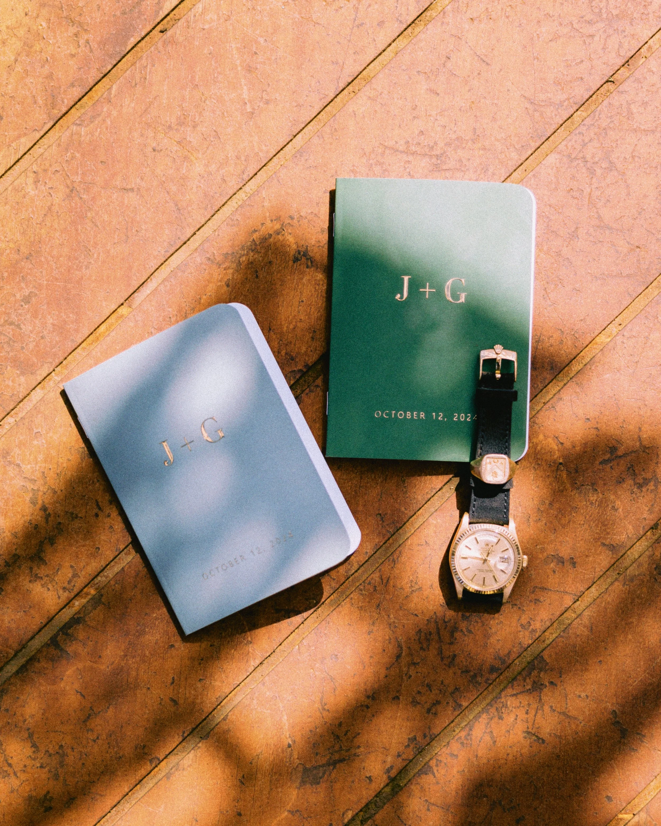 A flat lay of a watch, a closed cloth-covered book, and a small box with an elliptical shape on a wooden surface.