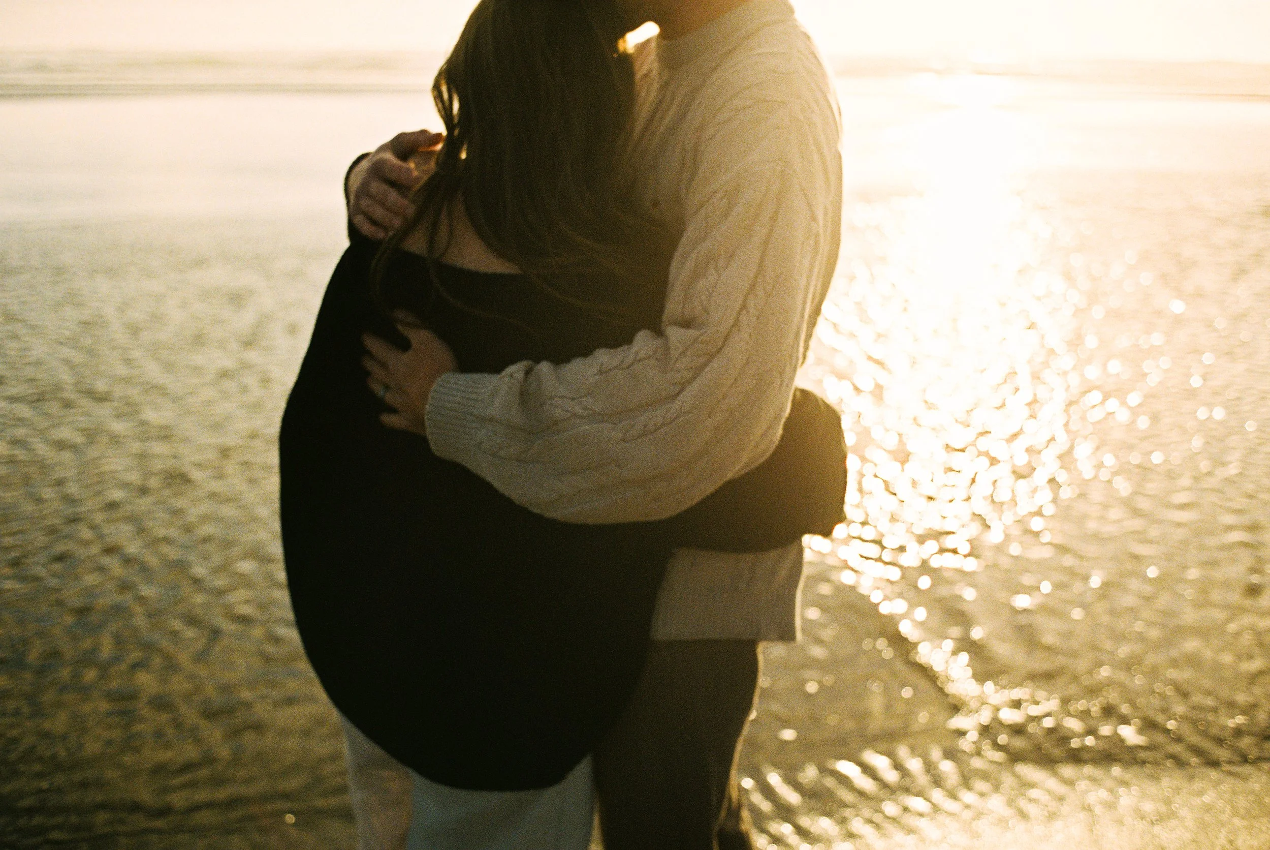 a couple hugging each other on film near the ocean with the sunset behind them
